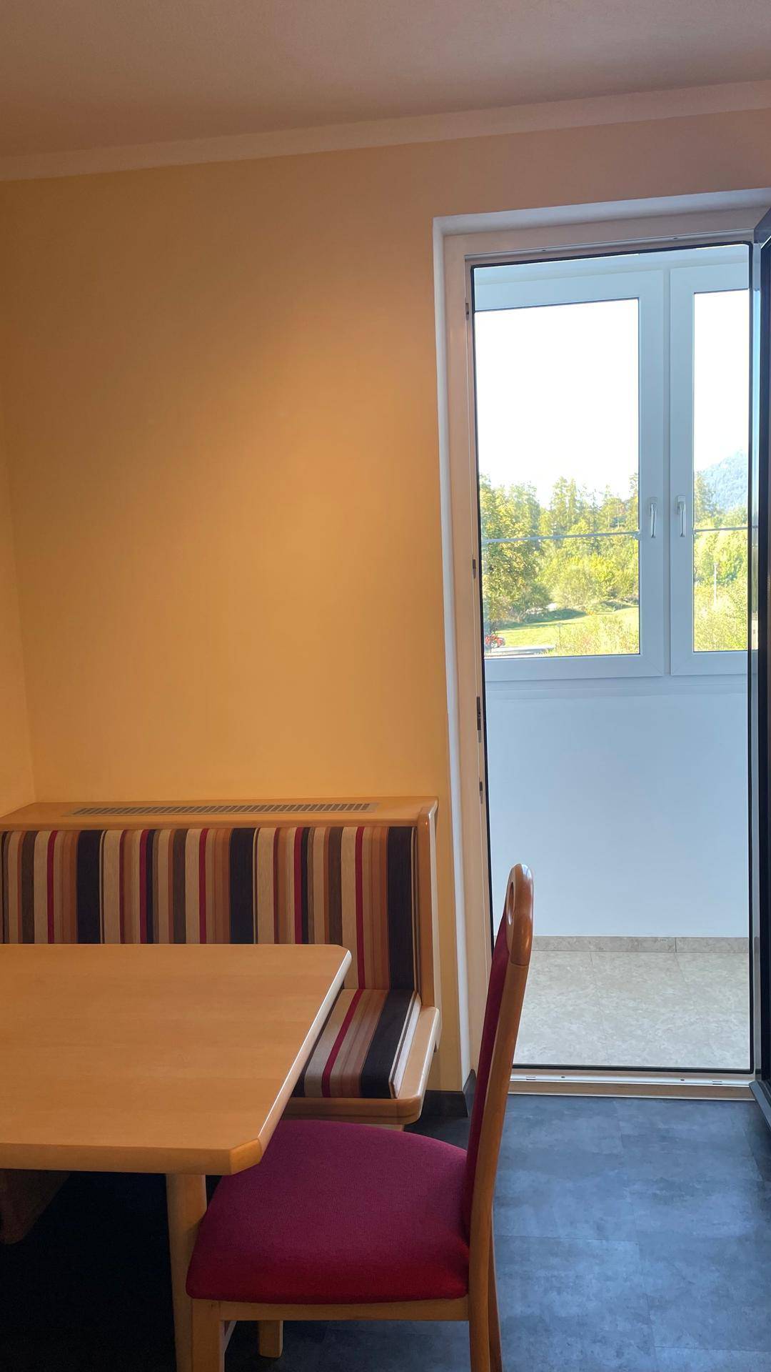 Gemütlicher Essbereich in der Küche mit Holztisch und Sitzbank, hell durch Balkontür.