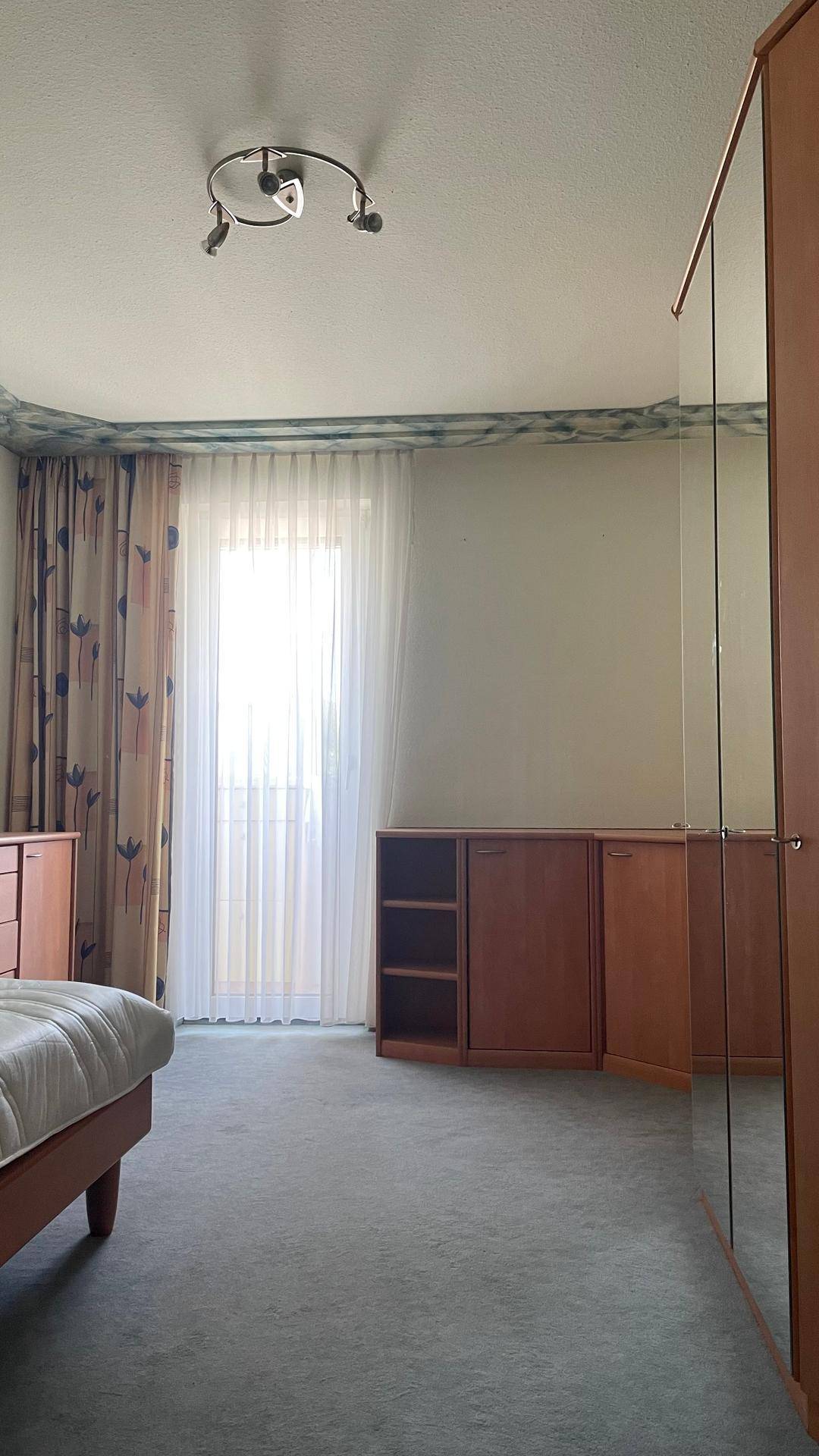 Schlafzimmer mit Teppichboden, Spiegelschrank und Zugang zu einem Balkon, hell und geräumig.