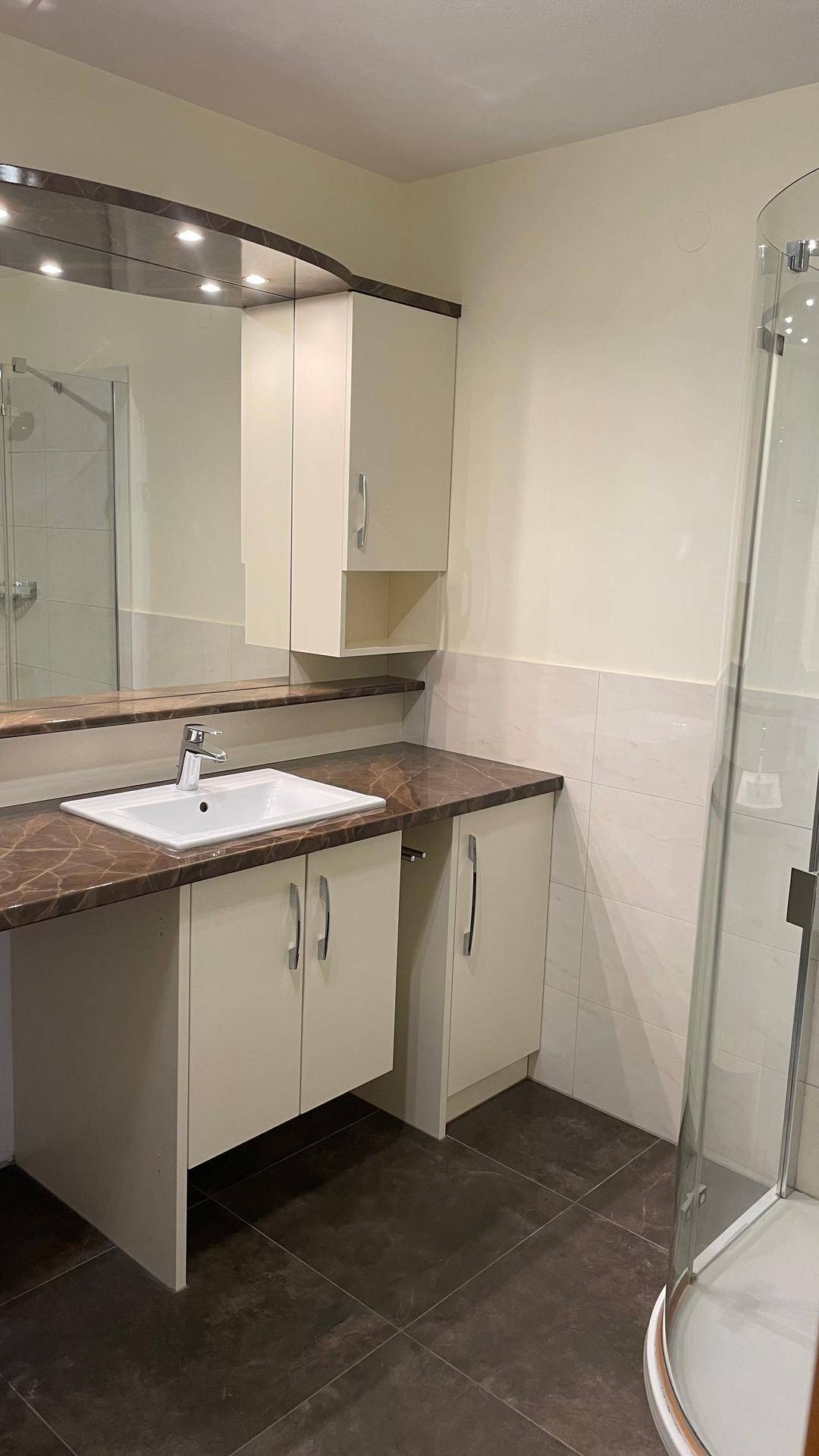 Funktionales Badezimmer mit Waschtischunterschrank, Spiegel und Eckdusche.