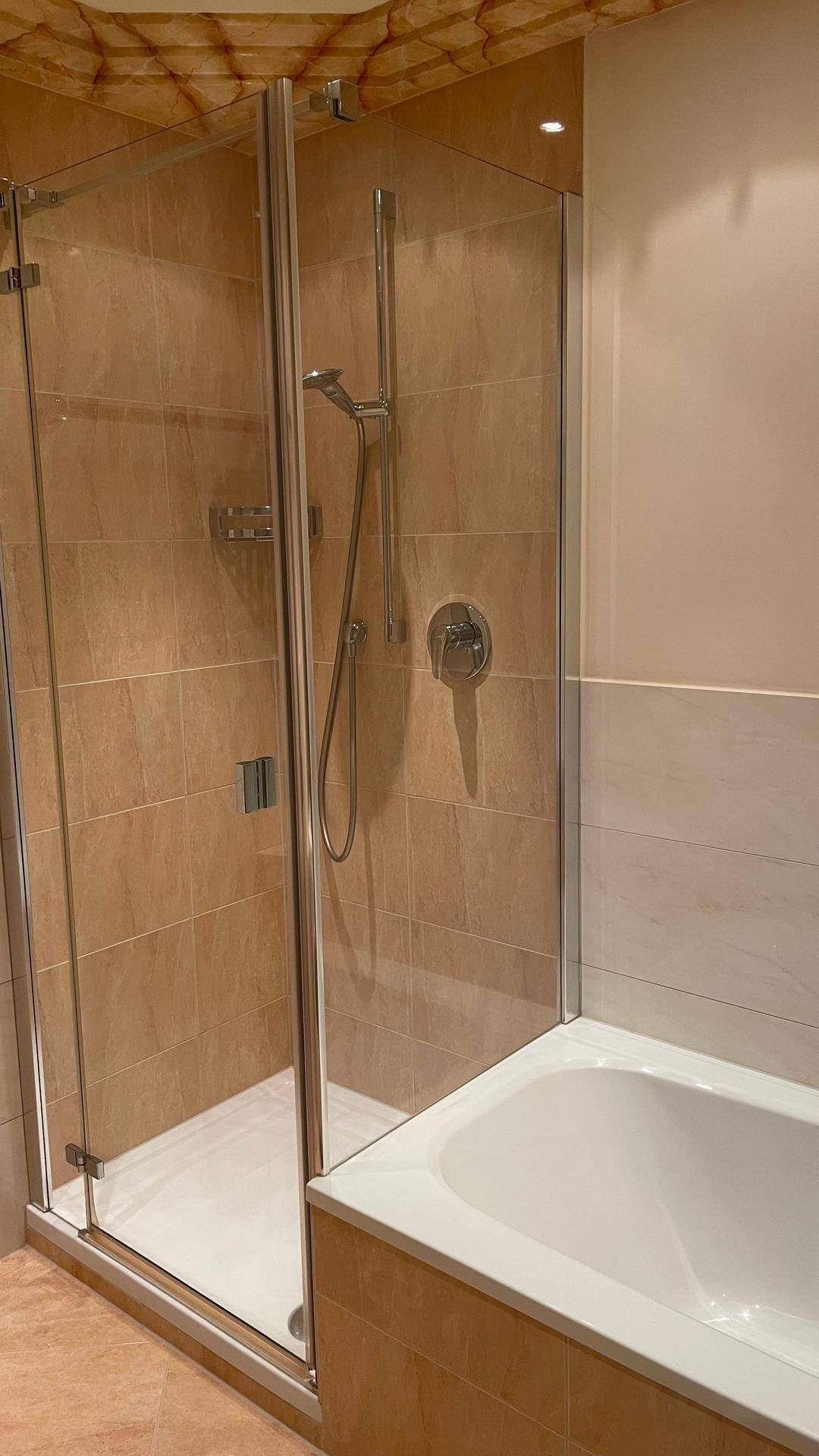 Badezimmer mit Duschkabine und Badewanne, ausgestattet mit hellen Fliesen und modernen Armaturen.