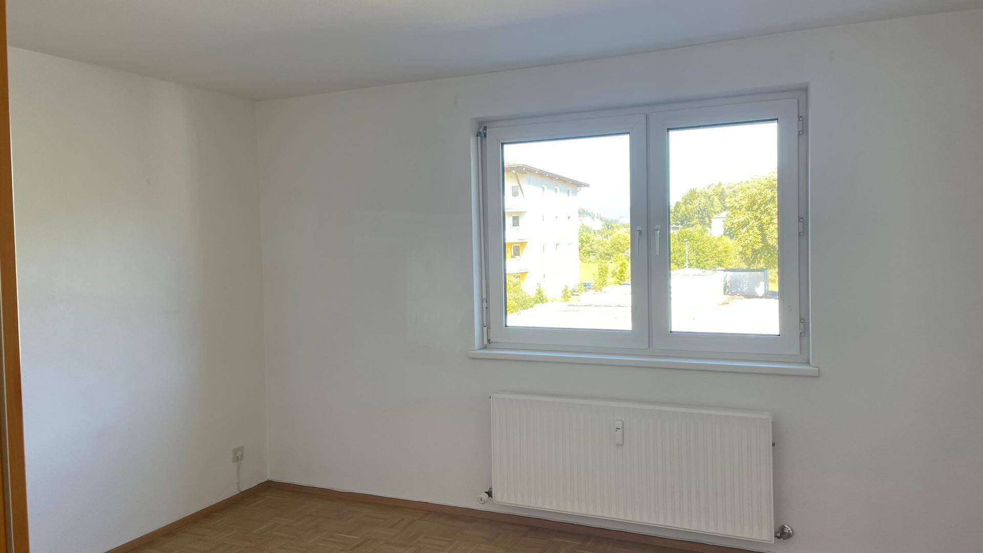 Leerer Raum mit Fenster, Heizkörper und Laminatboden, bereit zur individuellen Gestaltung.