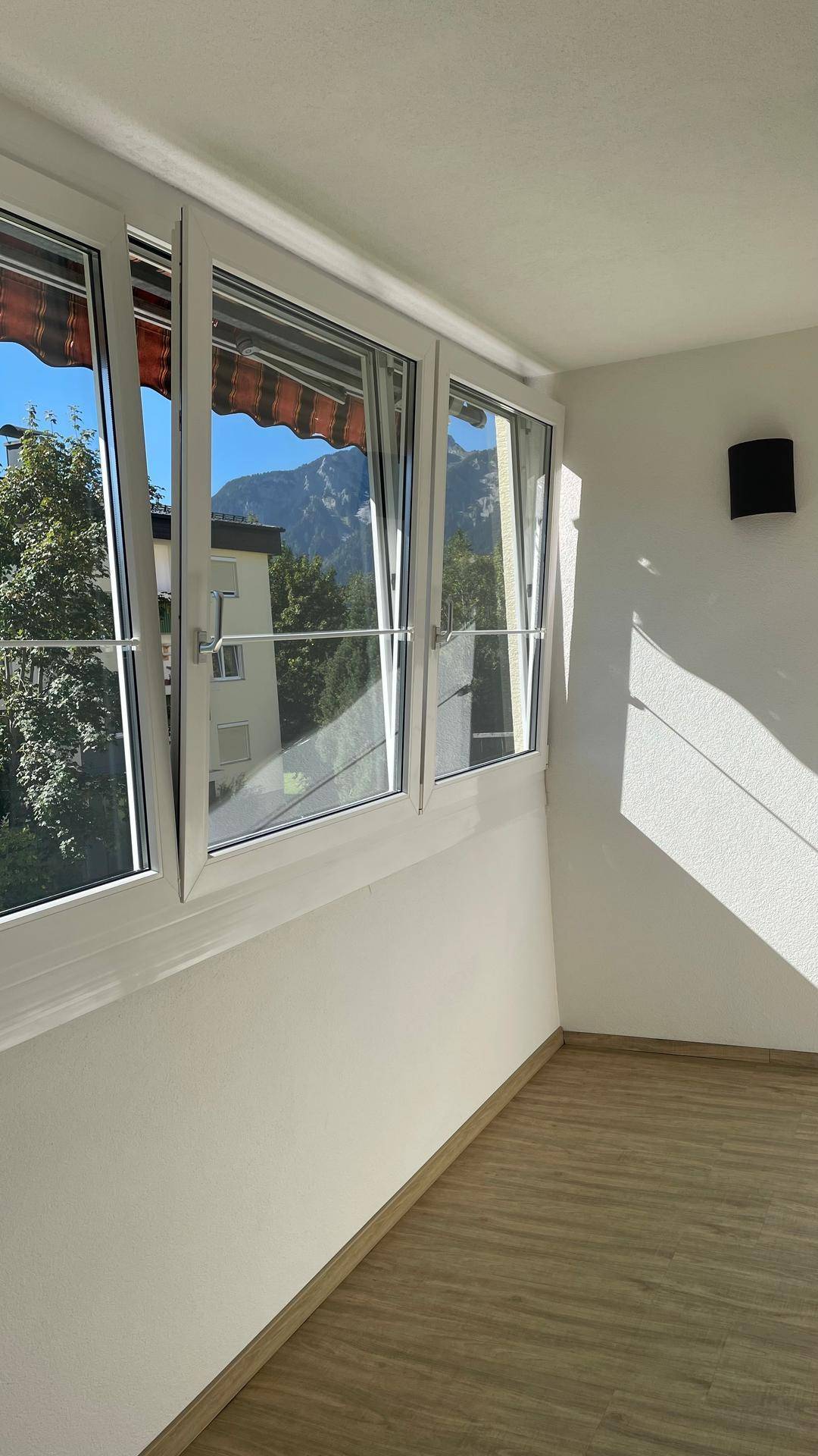 Lichtdurchflutete Loggia mit hellem Laminatboden und weitem Blick auf die Berglandschaft.