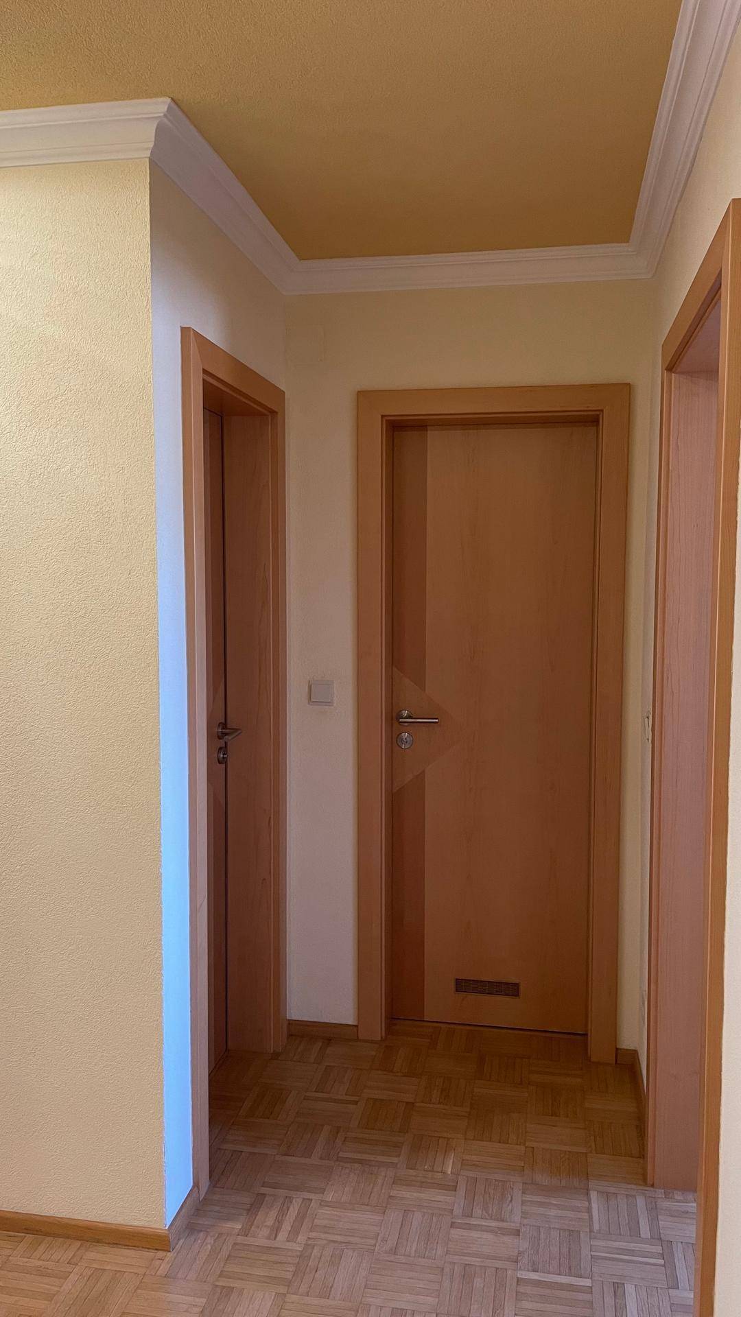 Flur mit mehreren Holztüren, Laminatboden und einer gelb gestrichenen Decke.