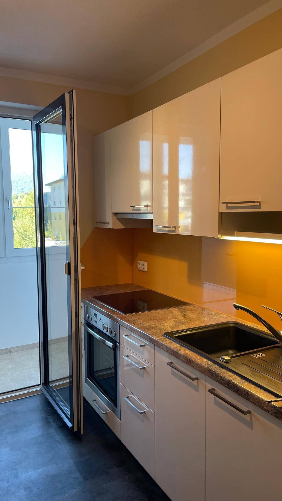 Moderne Einbauküche mit Kochfeld, Backofen und Spüle, direktem Balkonzugang.