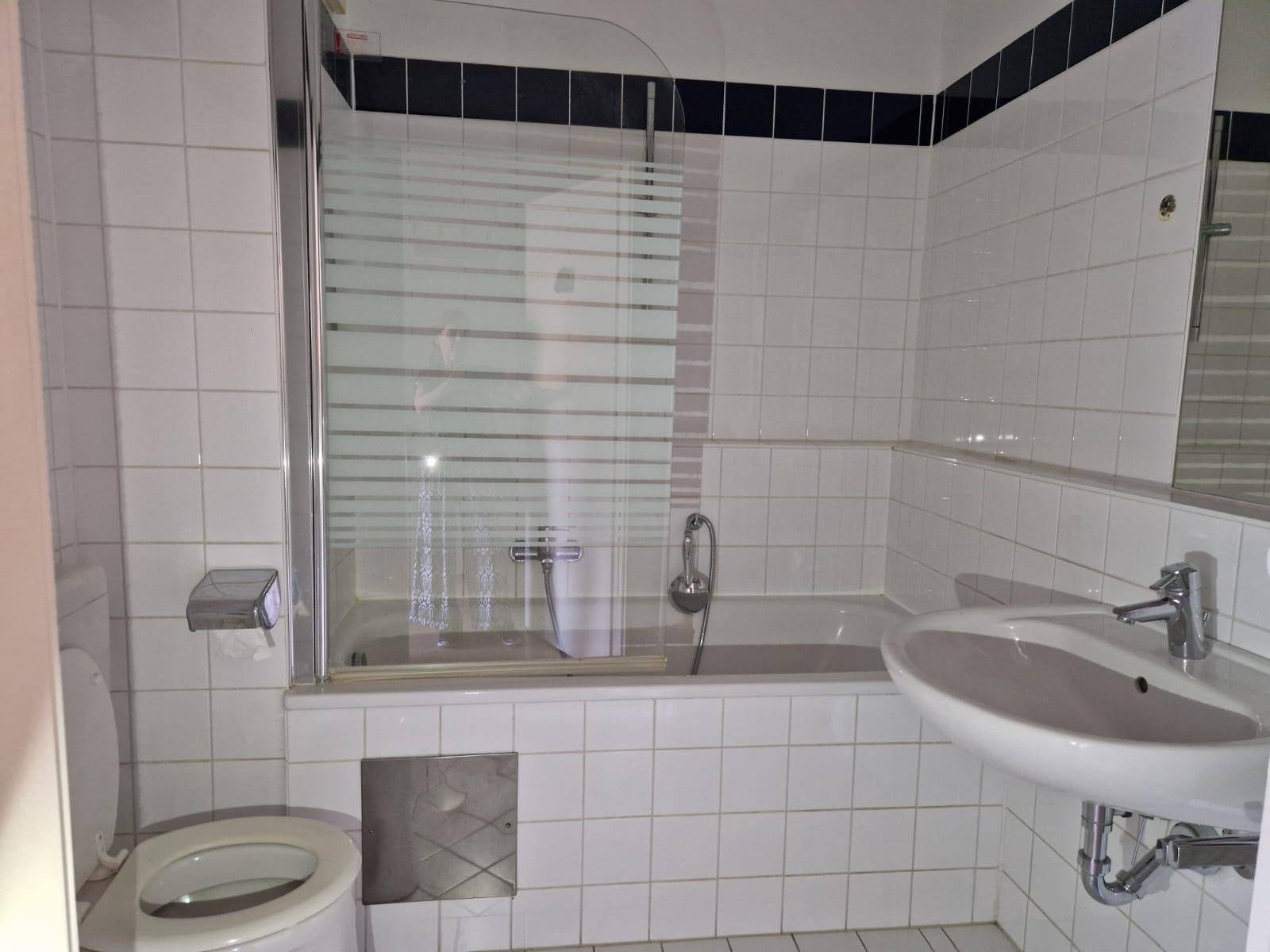 Gefliestes Badezimmer mit Badewanne, Duschabtrennung und Waschbecken in Weiß und Dunkelblau.
