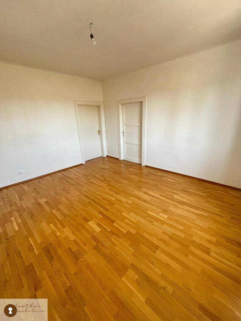 Geräumiger, heller Raum mit glänzendem Holzparkettboden und zwei weißen Türen.