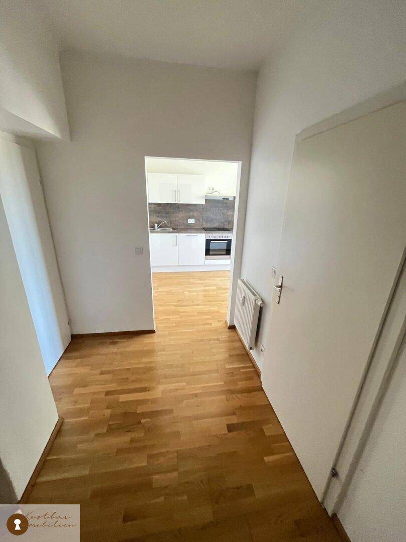 Heller Flur mit Holzparkettboden, der den Blick in die angrenzende Küche freigibt.