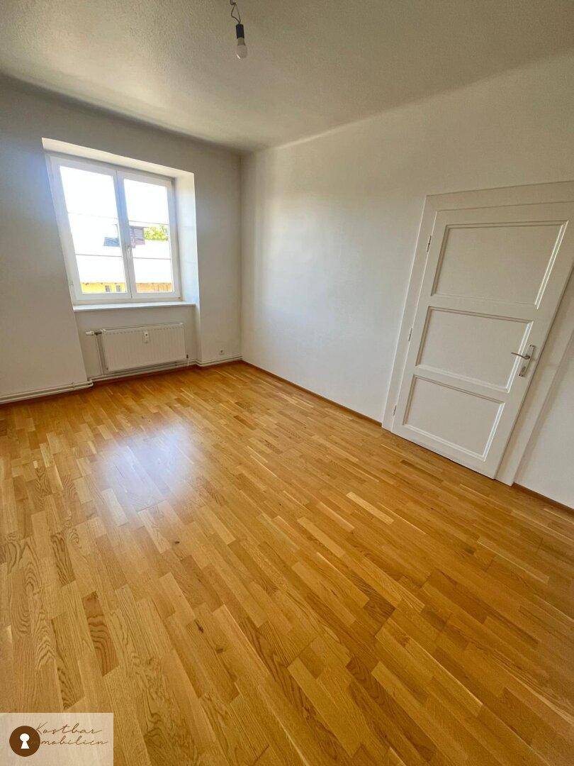 Lichtdurchflutetes Schlafzimmer mit klassischem Holzparkett und weiß gestrichenen Wänden.