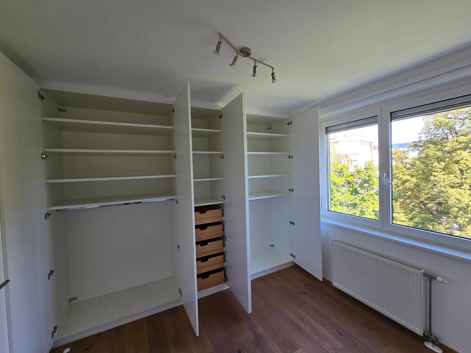 Schlafzimmer mit geöffneten Einbauschränken, die viel Stauraum bieten, neben einem Fenster.