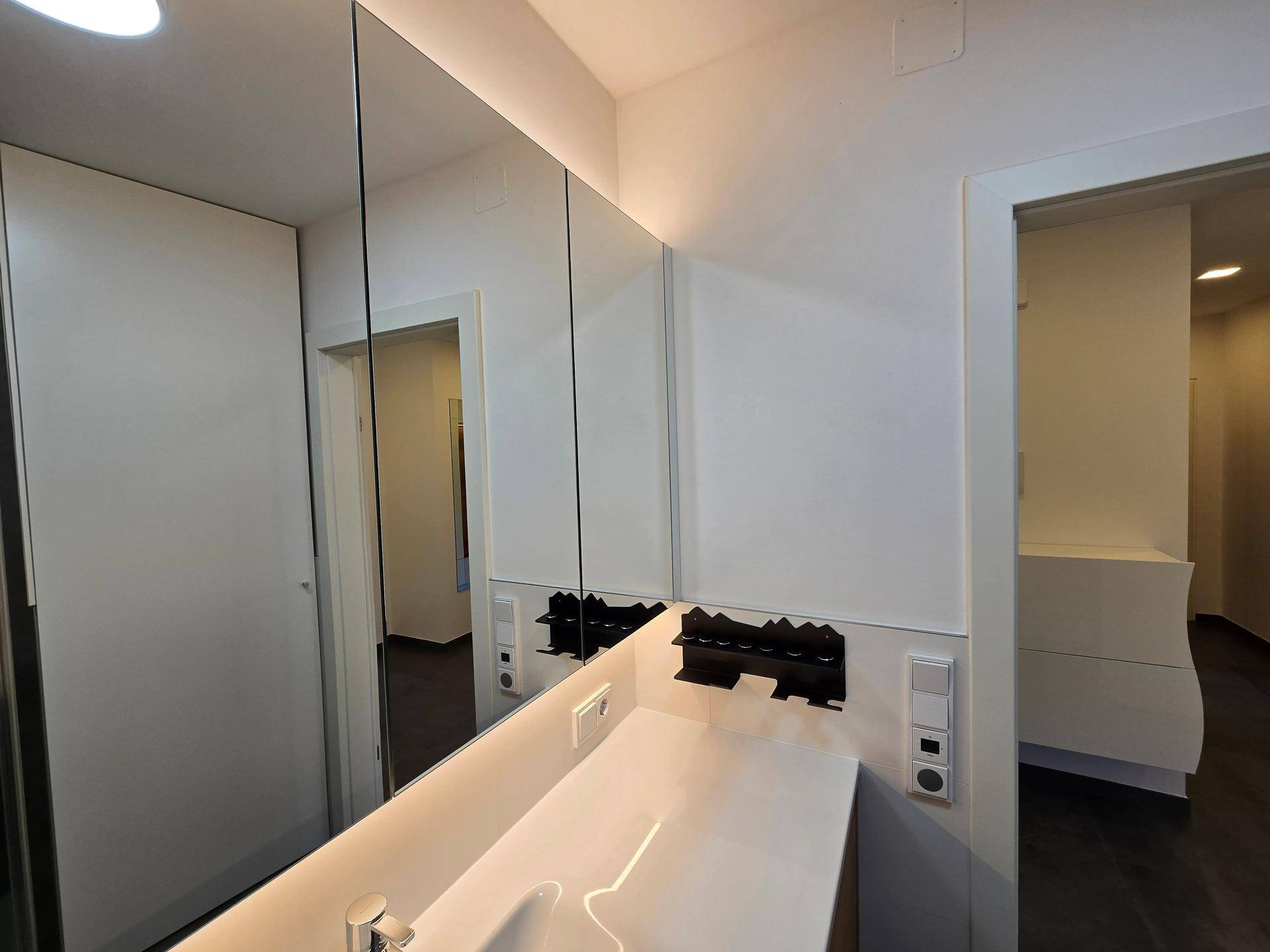 Modernes Badezimmer mit Waschtisch, Spiegelschrank und Blick in den Flur.