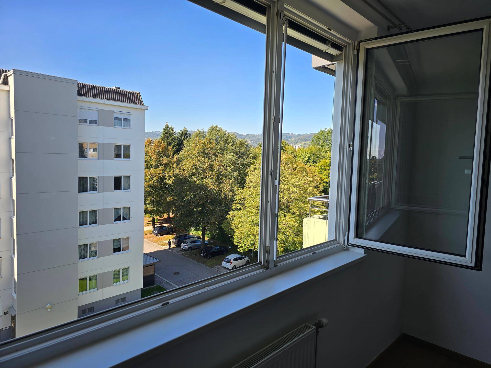 Fenster mit Blick auf ein Wohngebäude, Bäume und die umliegende Landschaft.