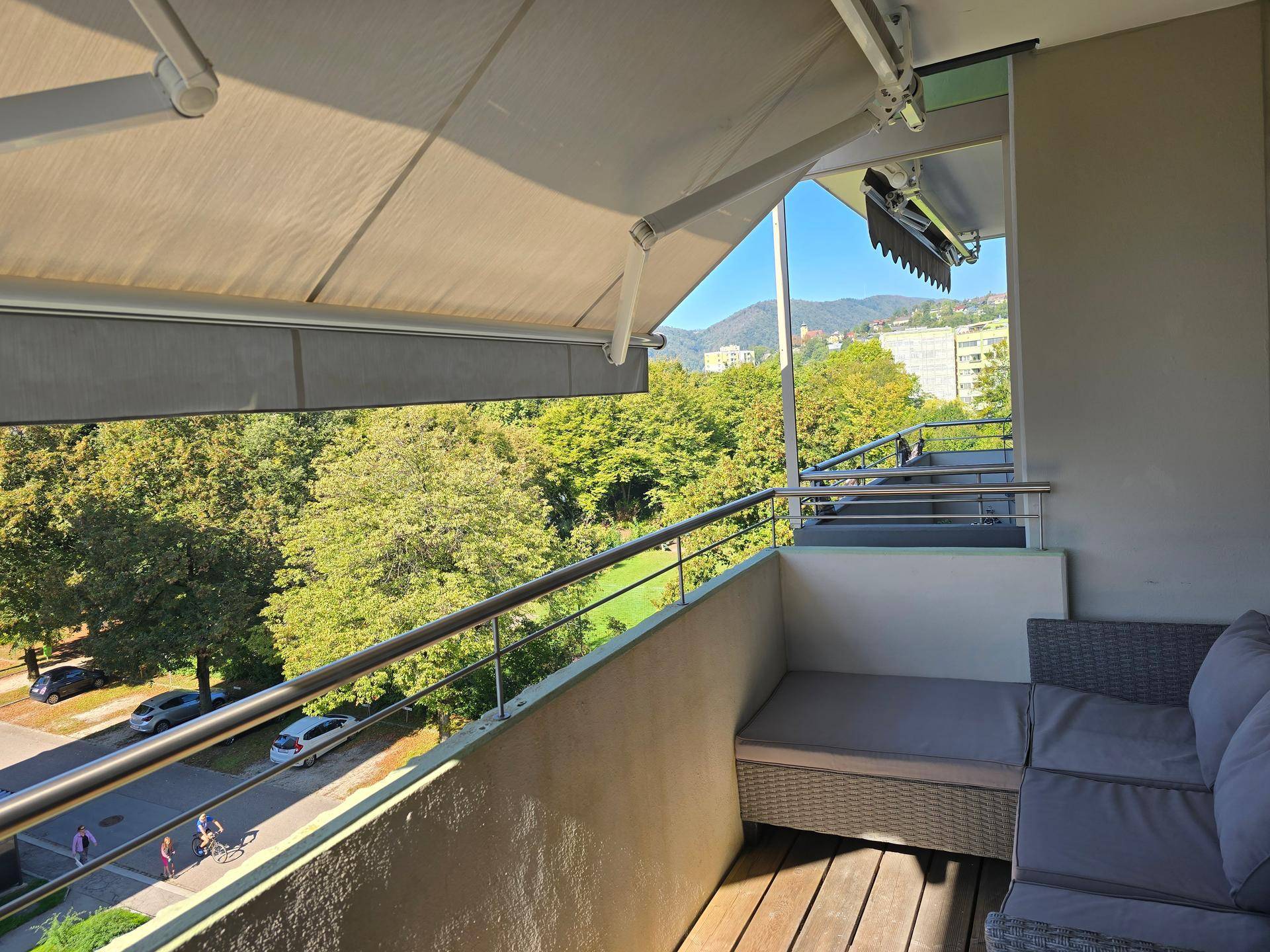 Sonniger Balkon mit Markise, Sitzgelegenheiten und Panoramablick auf die grüne Umgebung.