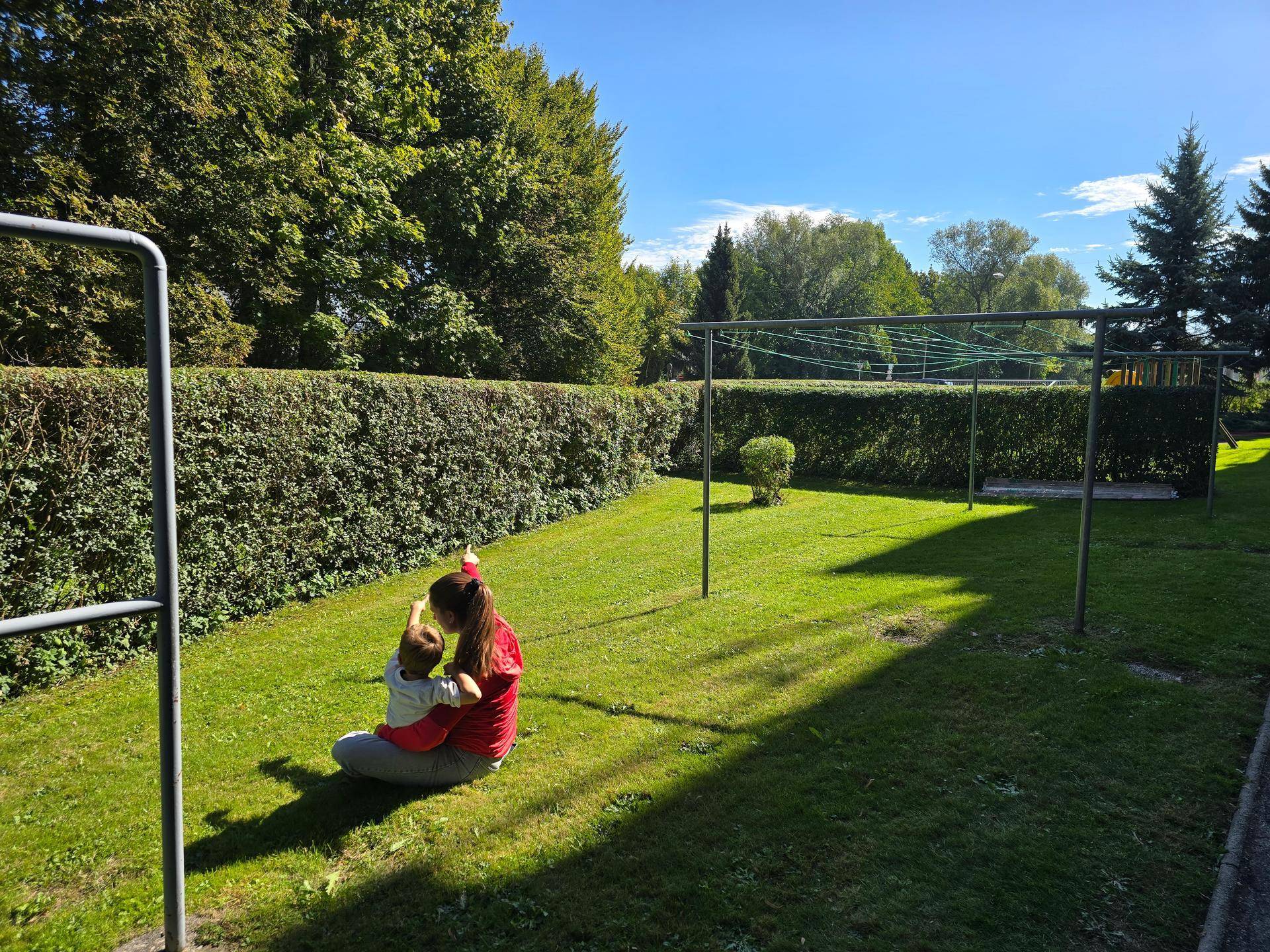 Sonniger Gemeinschaftsgarten mit Rasenfläche, Wäscheleinen und einer Familie im Grünen.