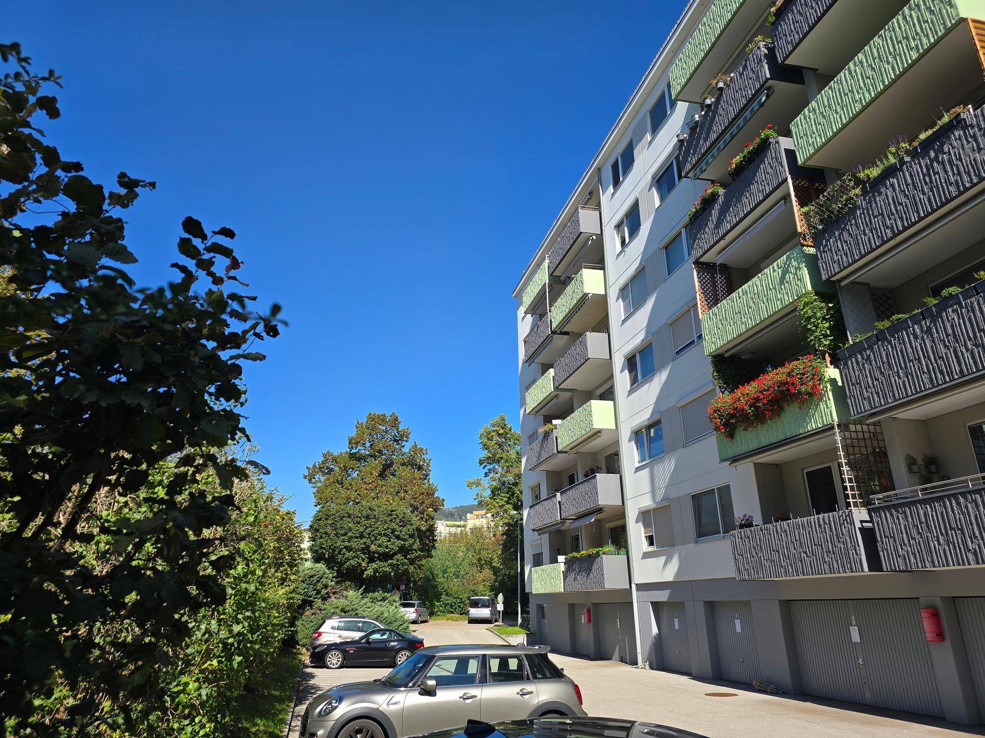 Fassade eines modernen Mehrfamilienhauses mit Balkonen, Blumenkästen und Garagen im Erdgeschoss.