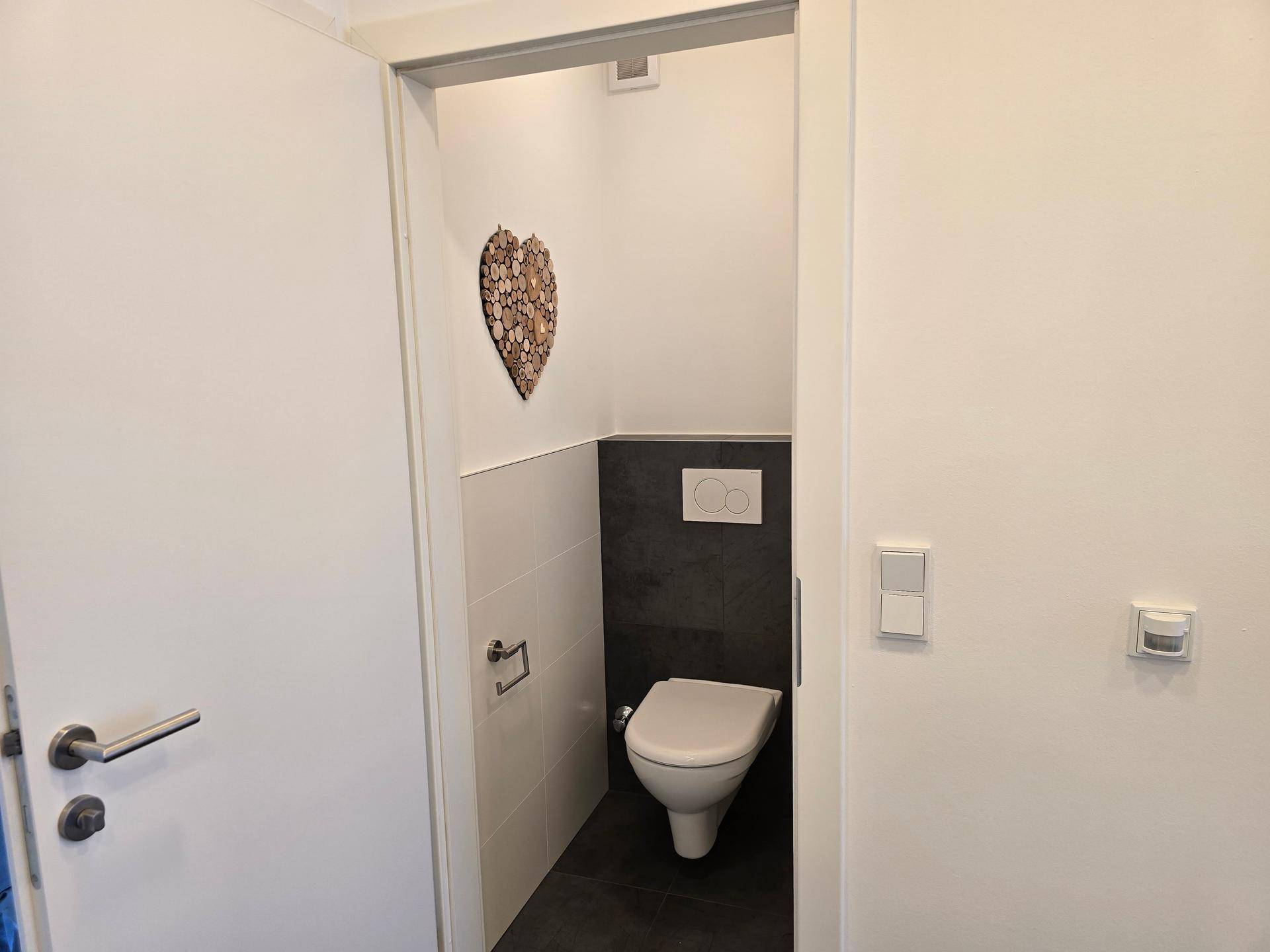 Gäste-WC mit moderner wandhängender Toilette und zweifarbigen Fliesen.