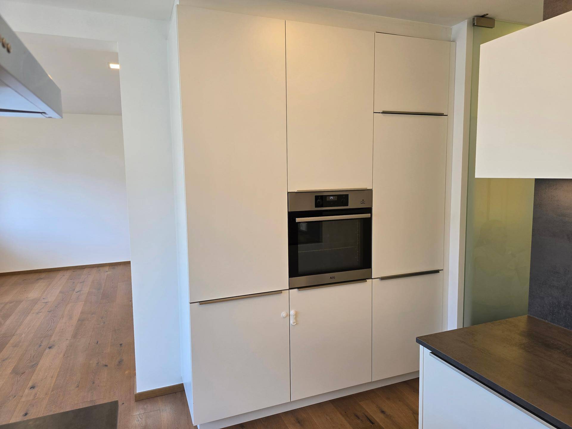 Hoher Küchenschrank mit integriertem Backofen und weißen, grifflosen Fronten.