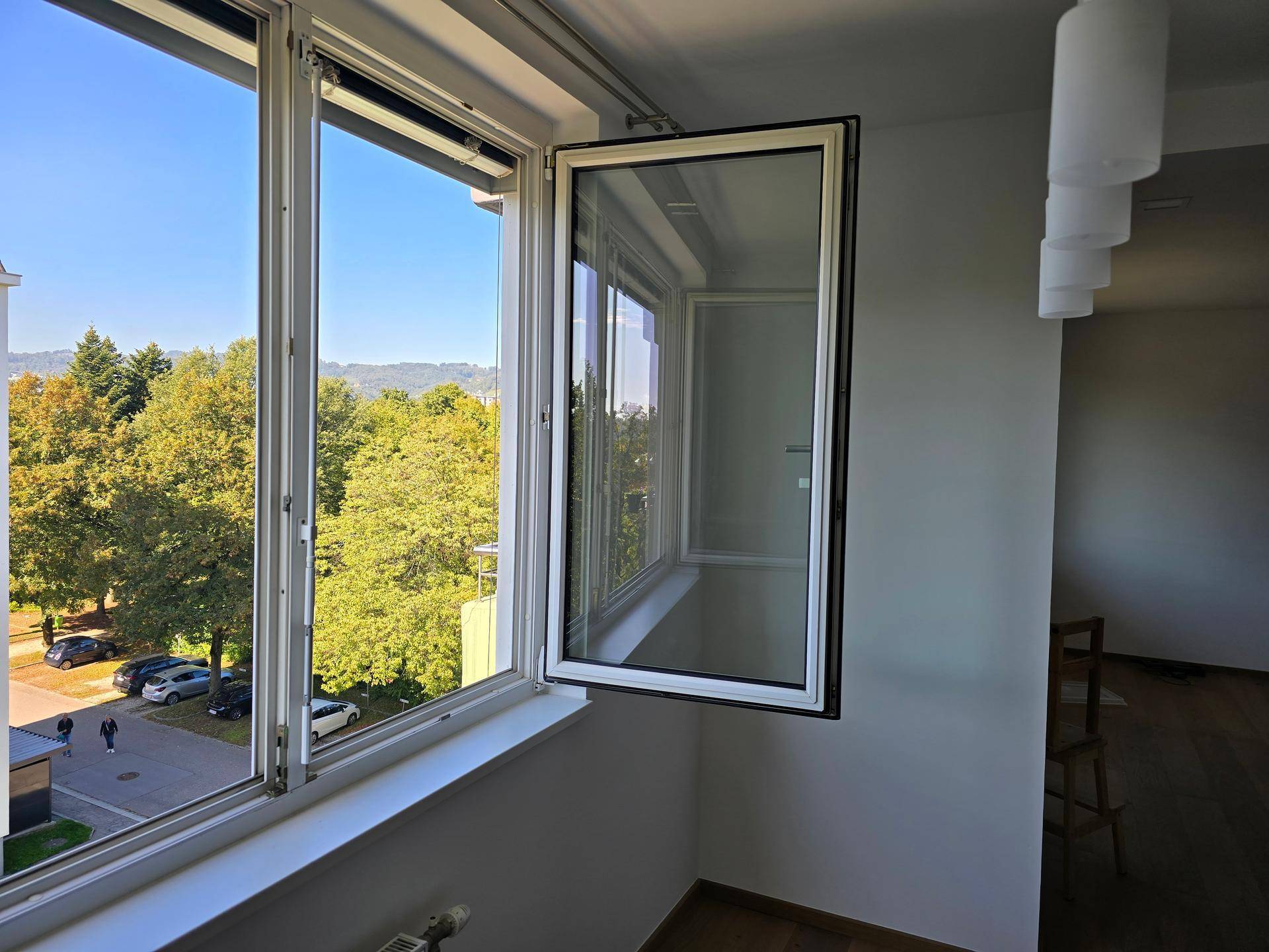 Großes Fenster mit Blick auf Bäume und die Umgebung, das viel Tageslicht hereinlässt.