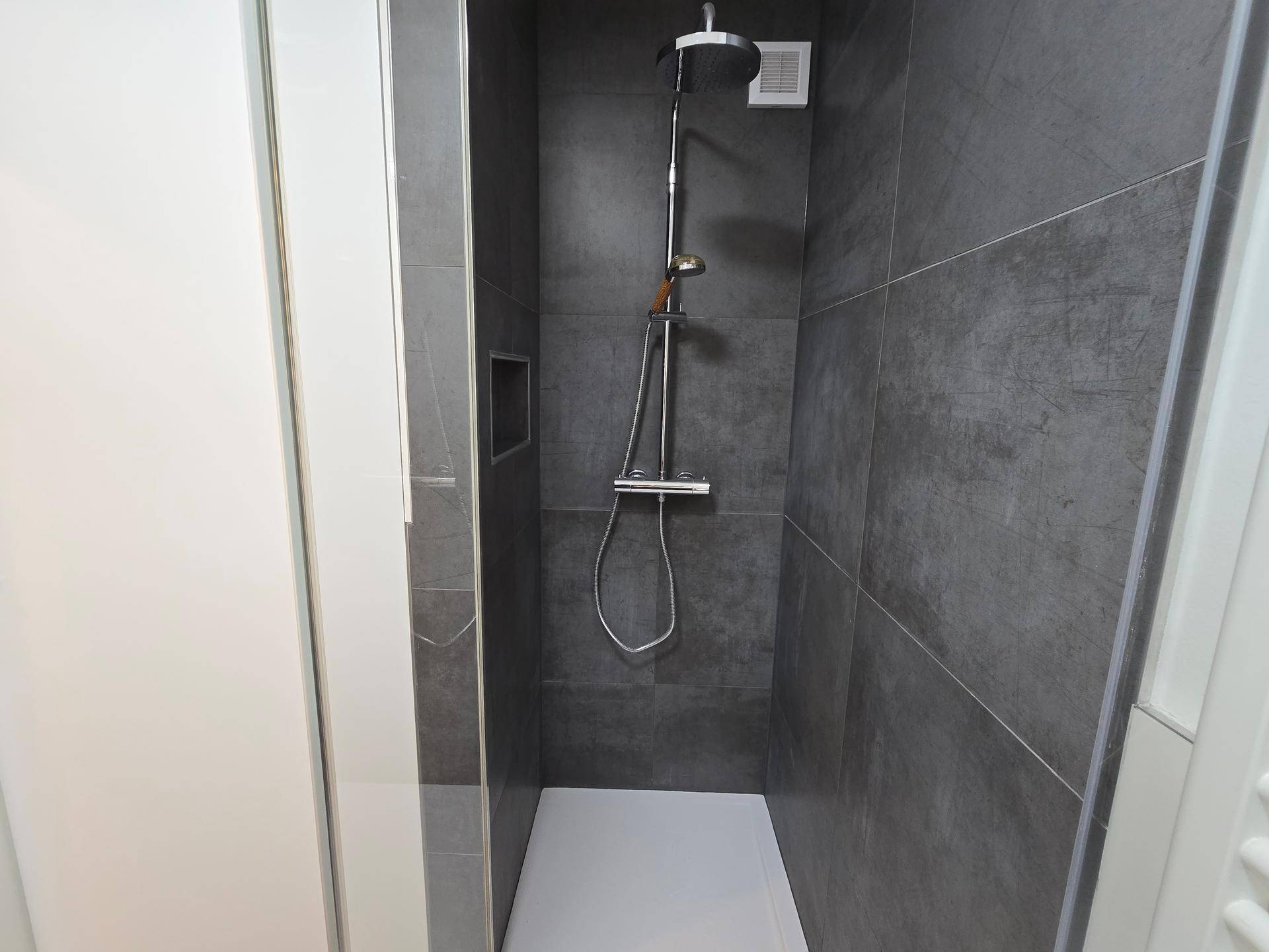 Moderne Duschkabine mit Regendusche, dunklen Fliesen und Duschwanne.