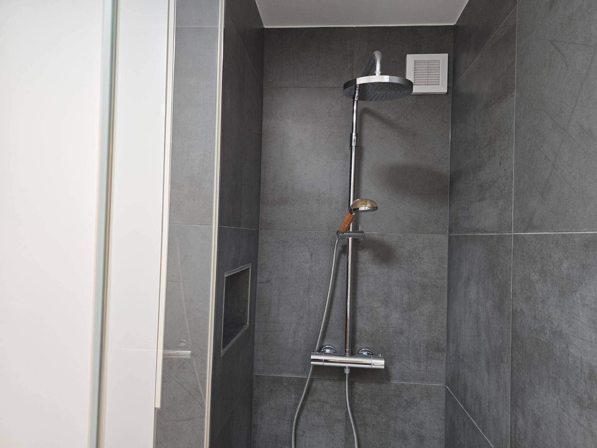 Moderne Duschkabine mit Regendusche, dunklen Fliesen und Ablagefach.