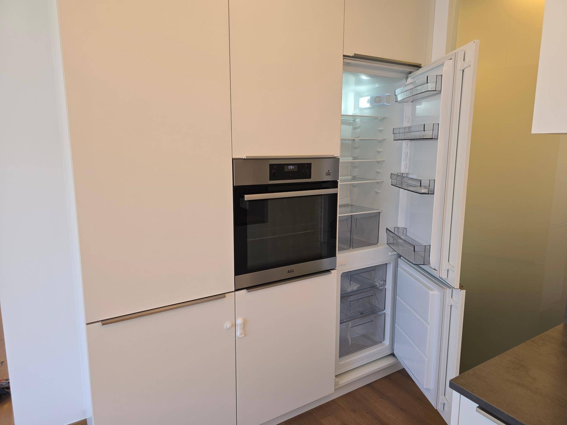 Integrierter Backofen und Kühlschrank in der modernen Einbauküche mit weißen Fronten.