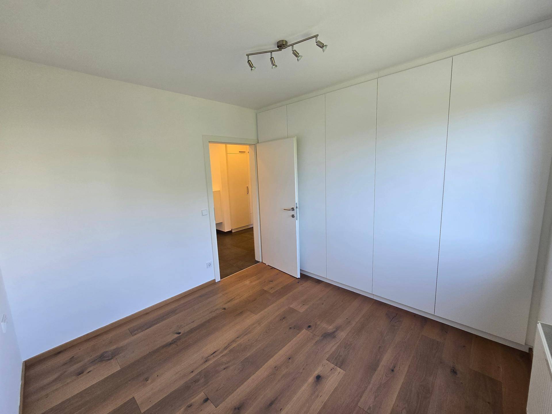 Schlafzimmer mit einer Wand voller weißer Einbauschränke und Holzboden.