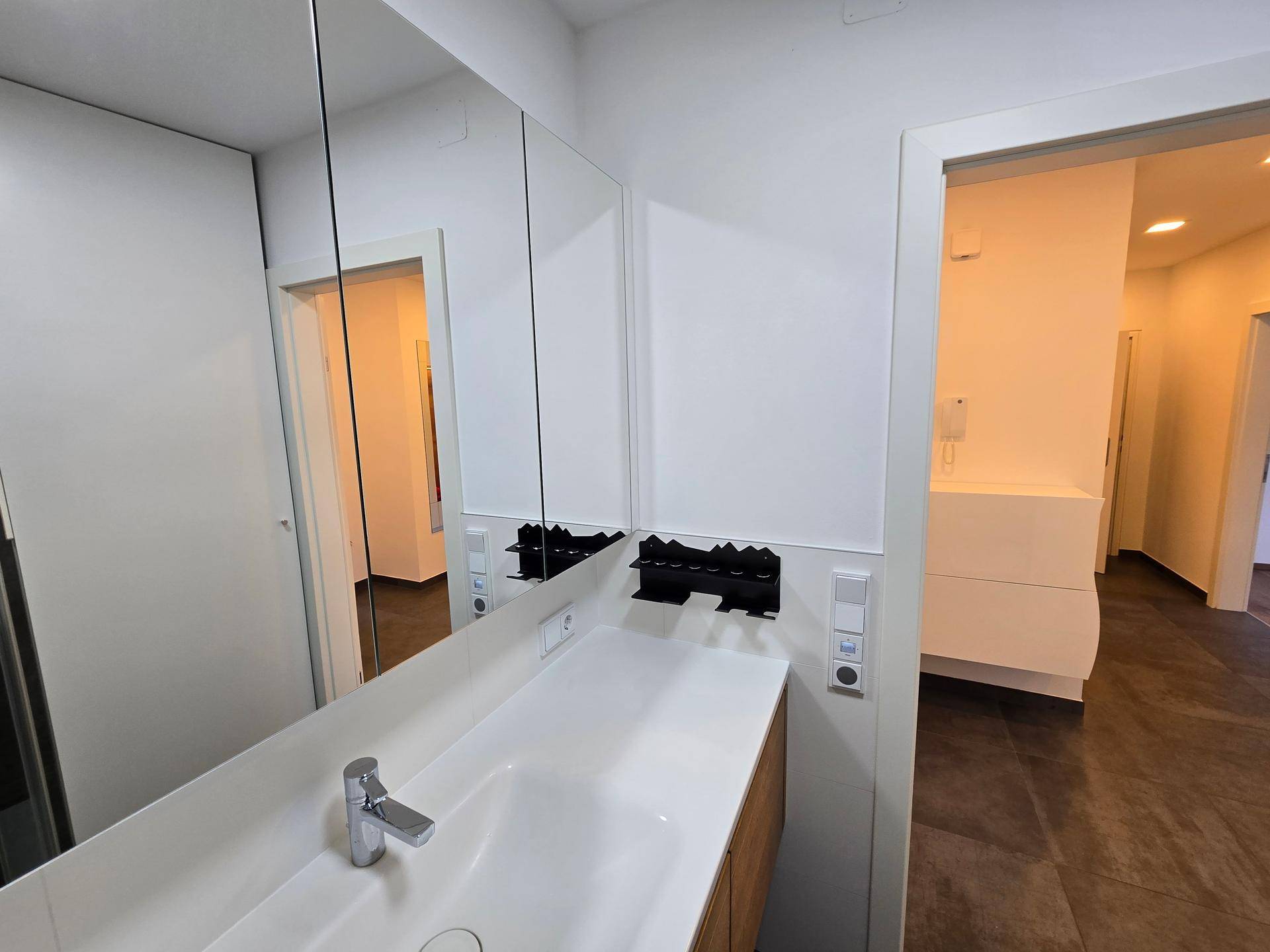 Modernes Badezimmer mit Waschtisch, Spiegelschrank und Blick in den angrenzenden Raum.