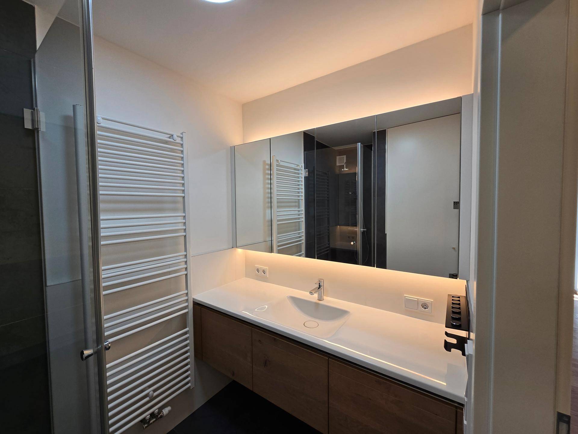 Modernes Badezimmer mit Waschtisch, großem Spiegel und integrierter Beleuchtung.