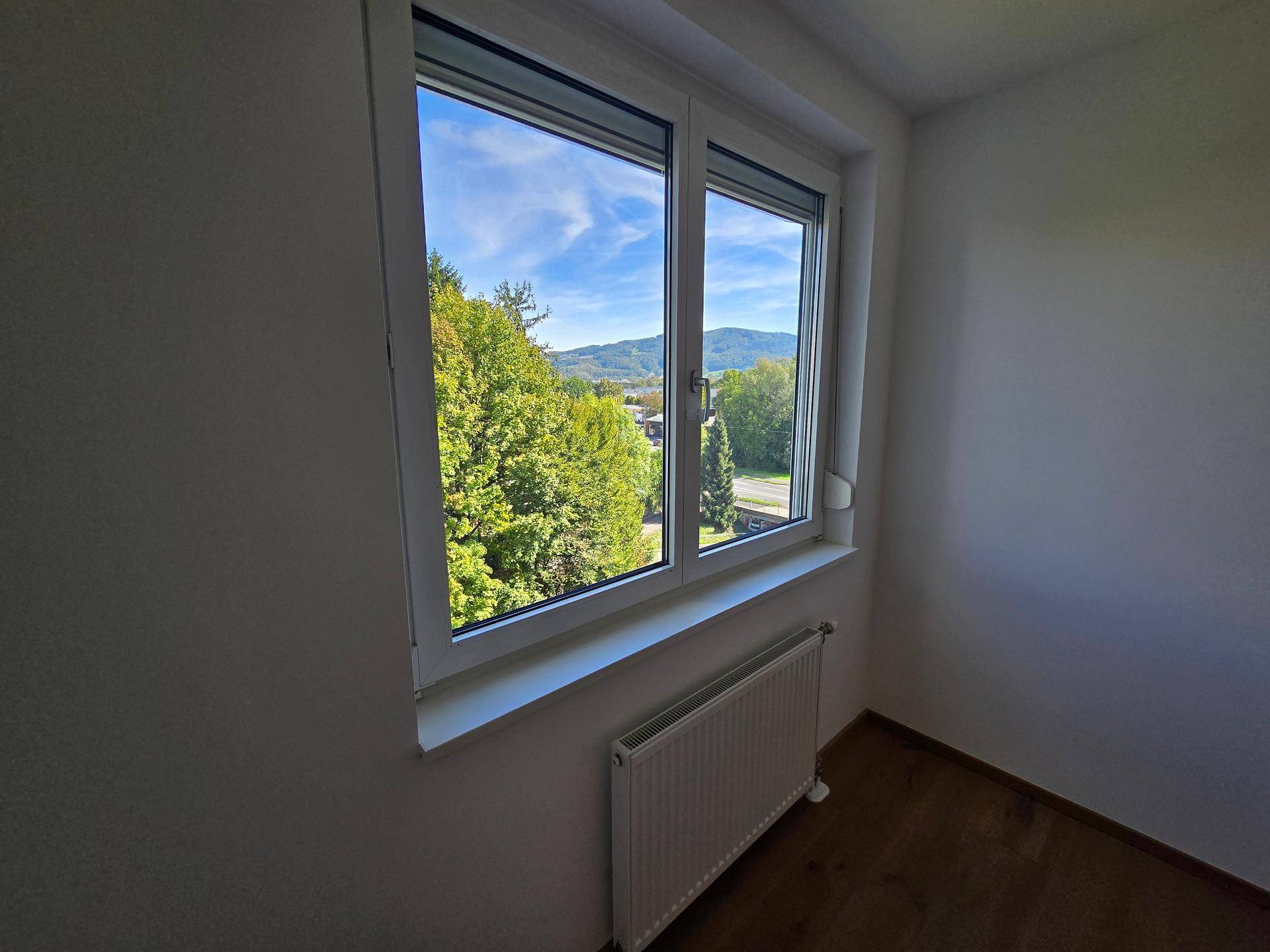 Fenster mit weitem Blick auf grüne Bäume und die umliegende Hügellandschaft.