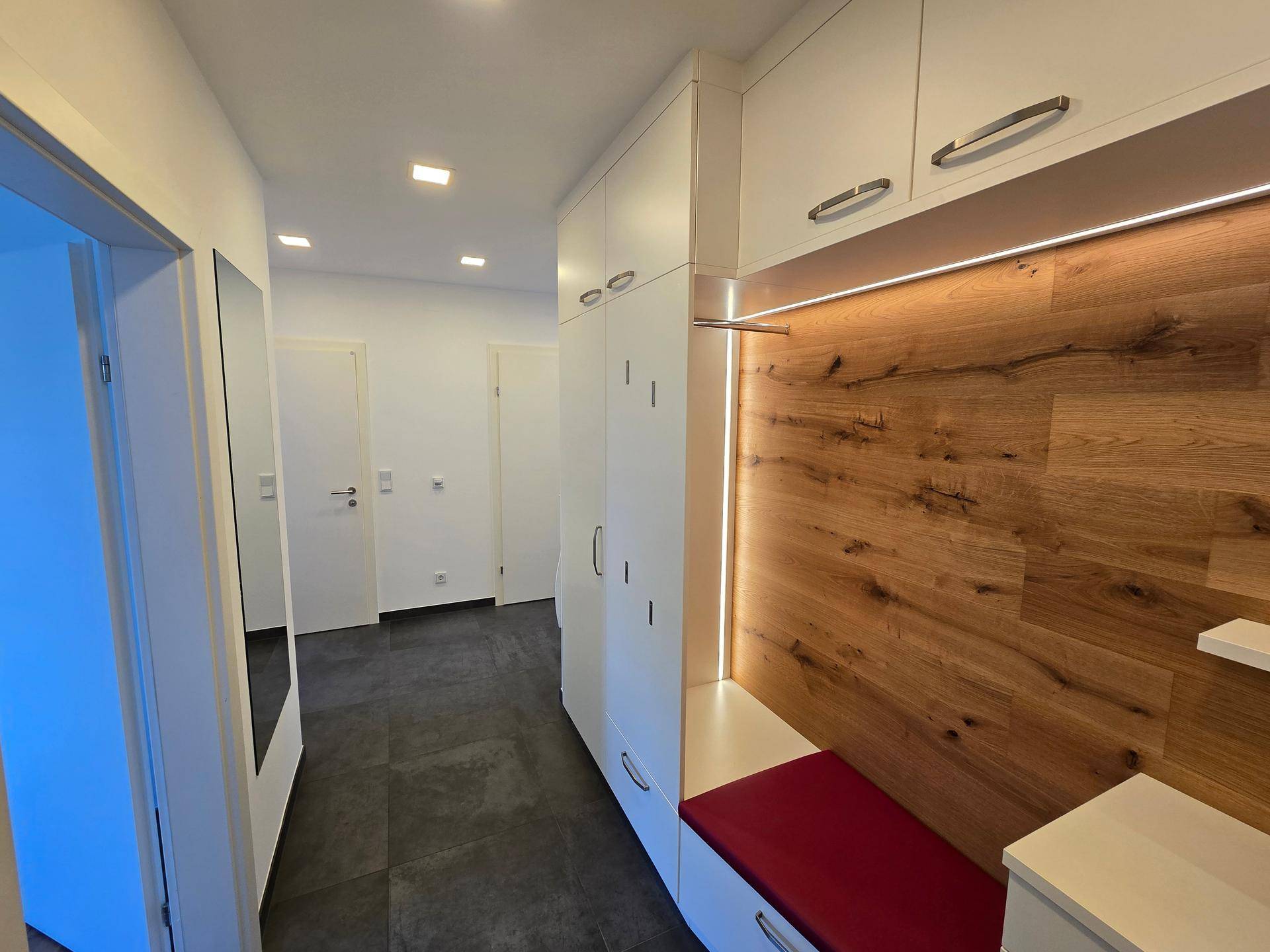 Langer Flur mit integrierter Garderobe, Holzelementen und dunklem Fliesenboden.