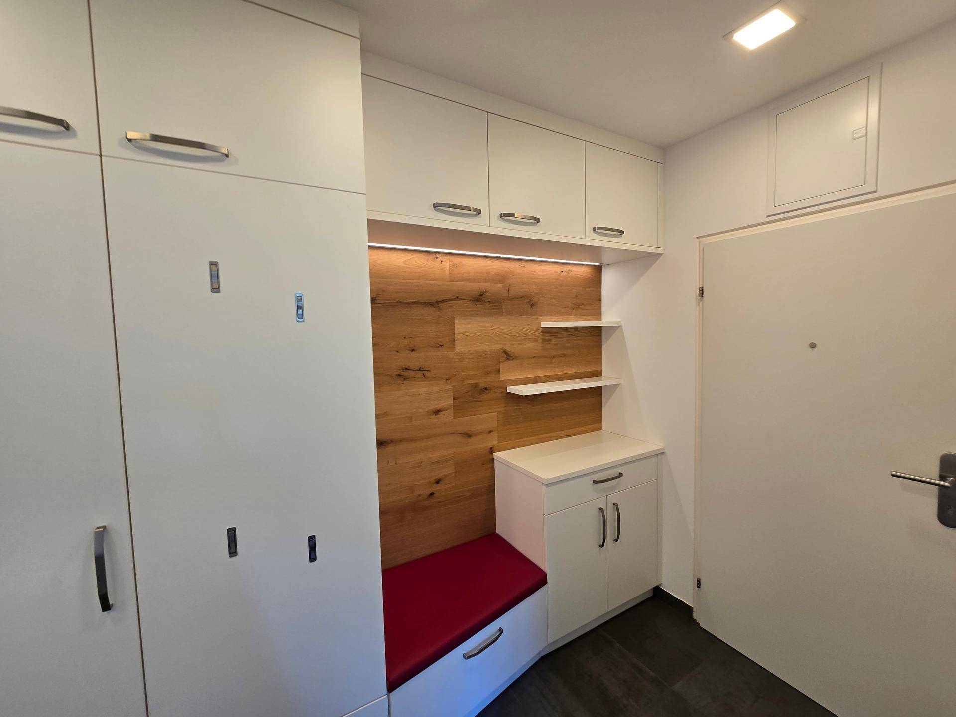 Detailansicht der Garderobe im Flur mit Holzakzenten, Sitzbank und integrierter Beleuchtung.