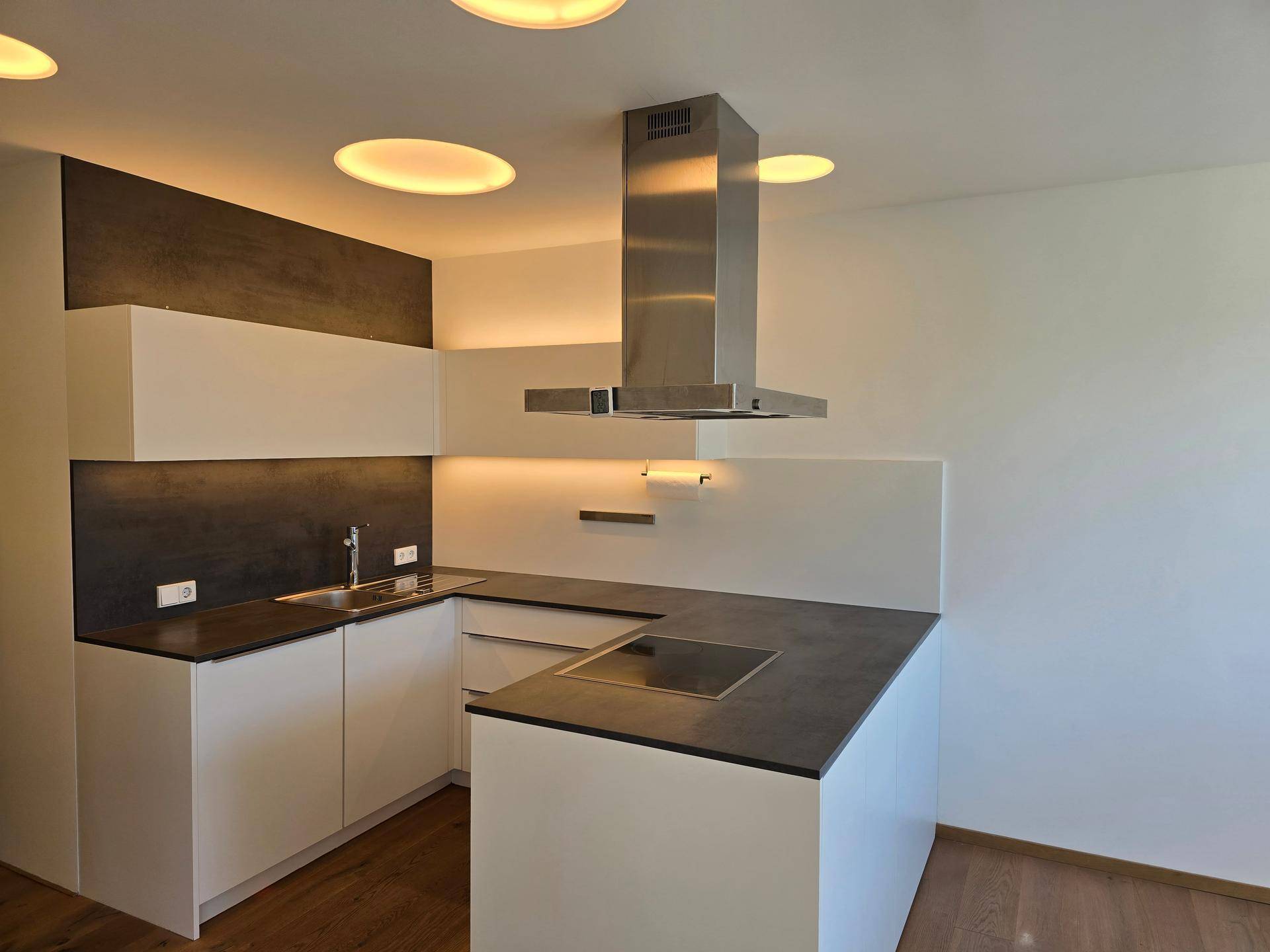 Moderne Einbauküche mit weißen Schränken, dunkler Arbeitsplatte und Dunstabzugshaube.
