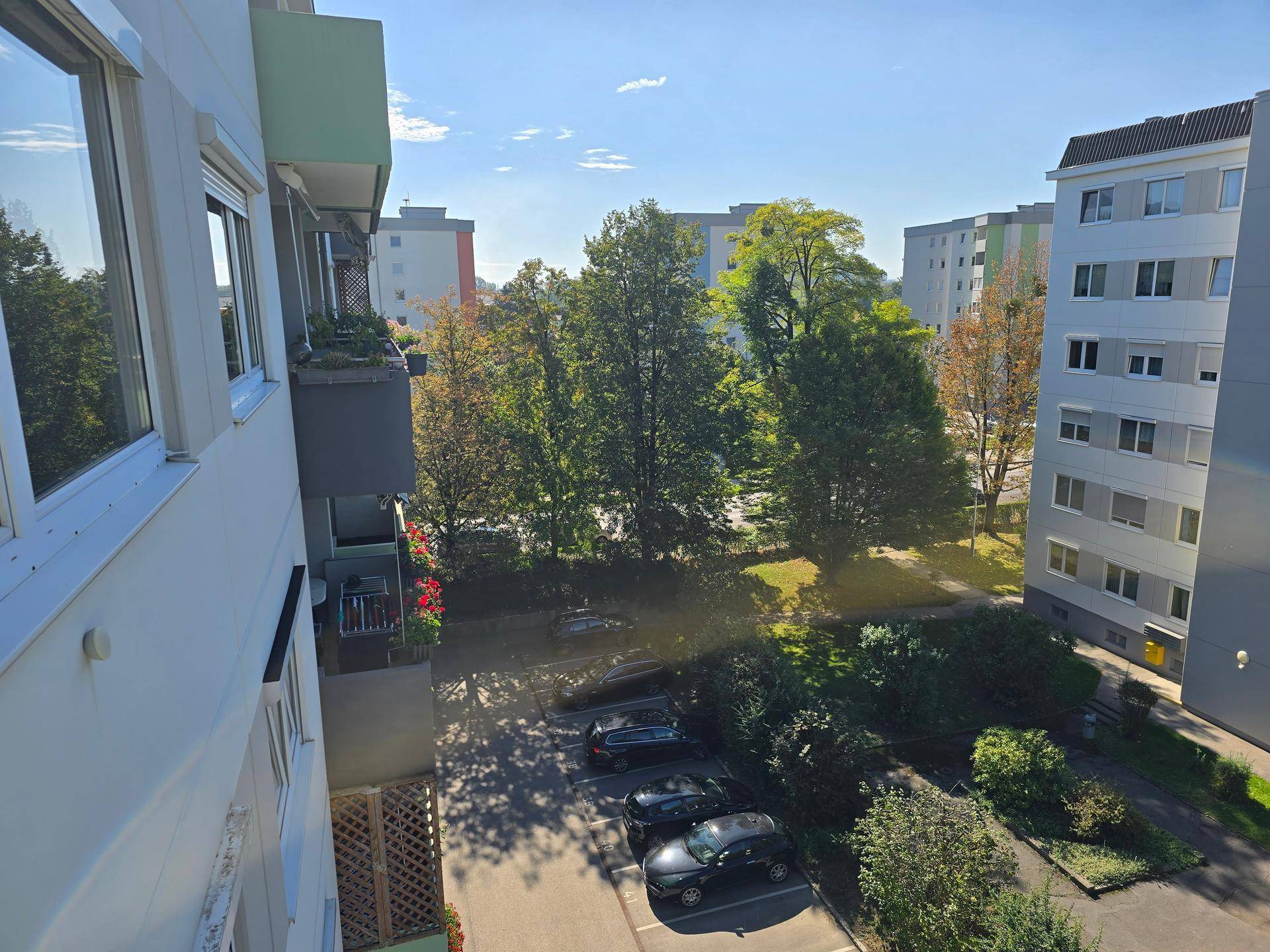 Ausblick vom Balkon auf die grüne Wohnanlage mit Parkplätzen und umliegenden Gebäuden.