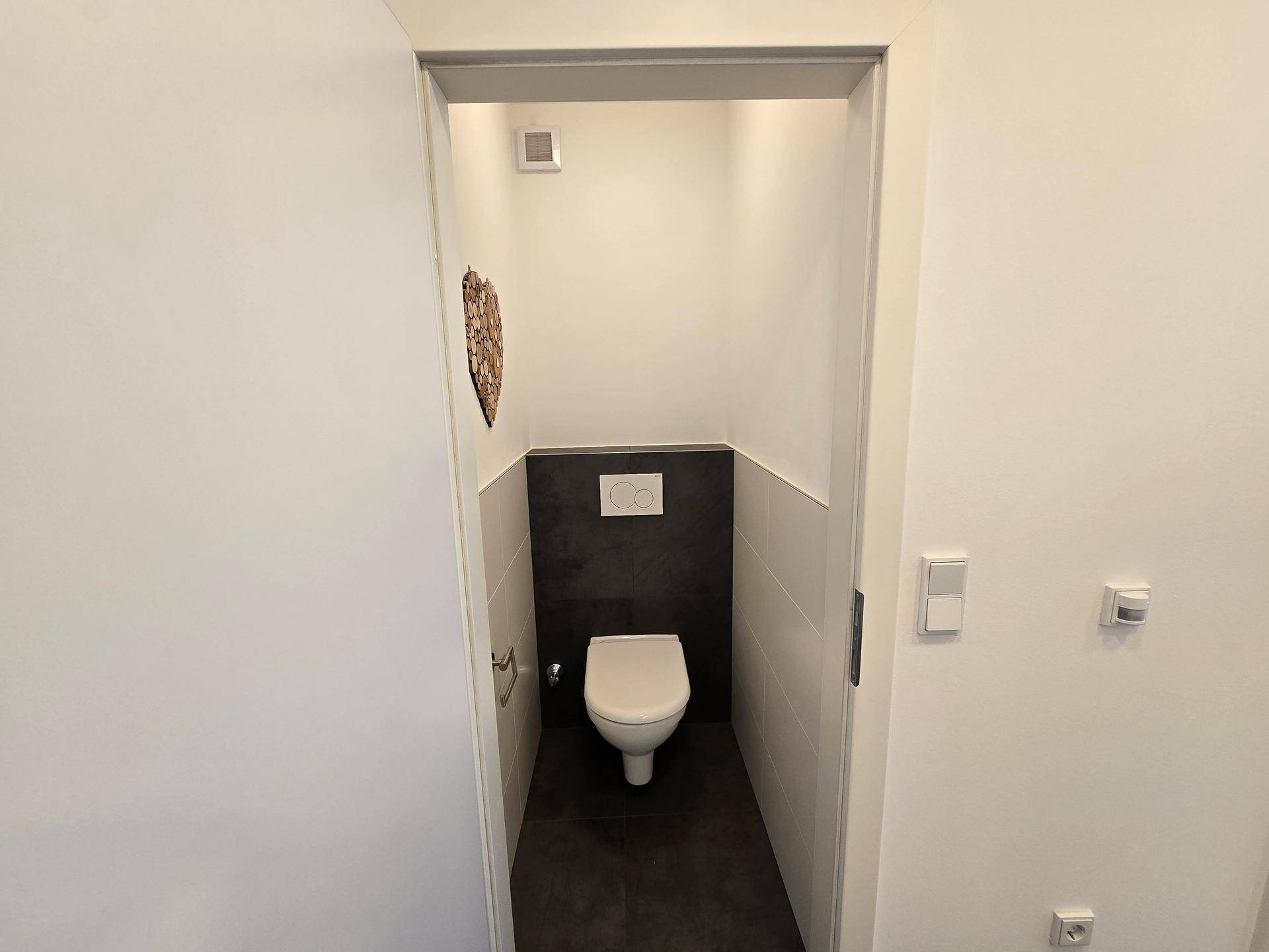 Modernes Gäste-WC mit wandhängender Toilette und stilvollen Fliesen in dunklen und hellen Tönen.
