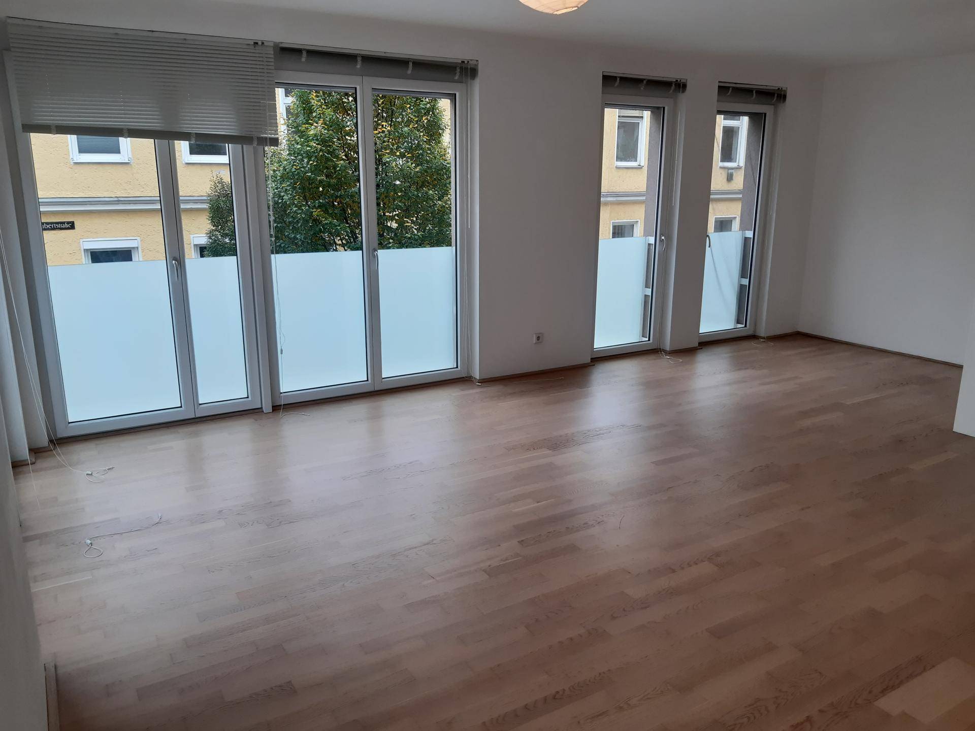 Geräumiger Raum mit Holzboden und mehreren bodentiefen Fenstern, die viel natürliches Licht hereinlassen.