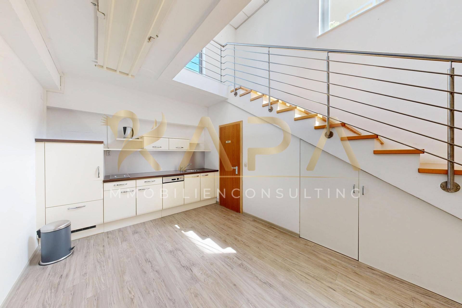 Küchenzeile unter einem Treppenaufgang mit Holzstufen und Edelstahlgeländer, heller Laminatboden.