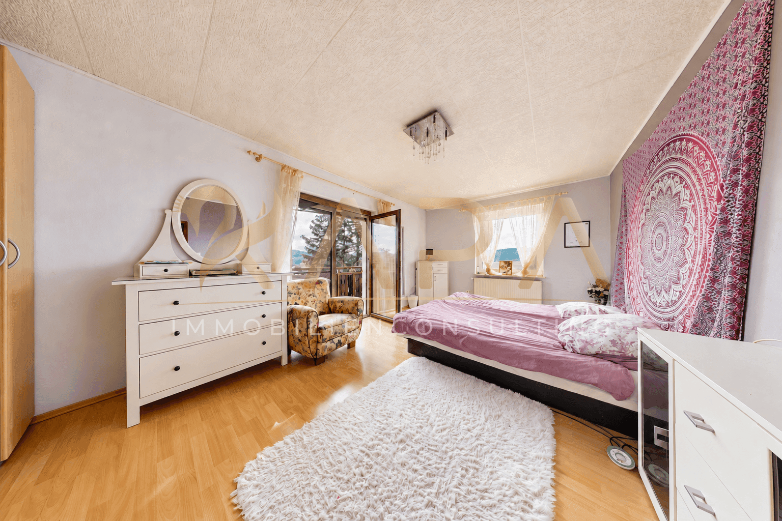 Schlafzimmer mit Holzboden, Kommode, Doppelbett und Zugang zu einem Balkon.