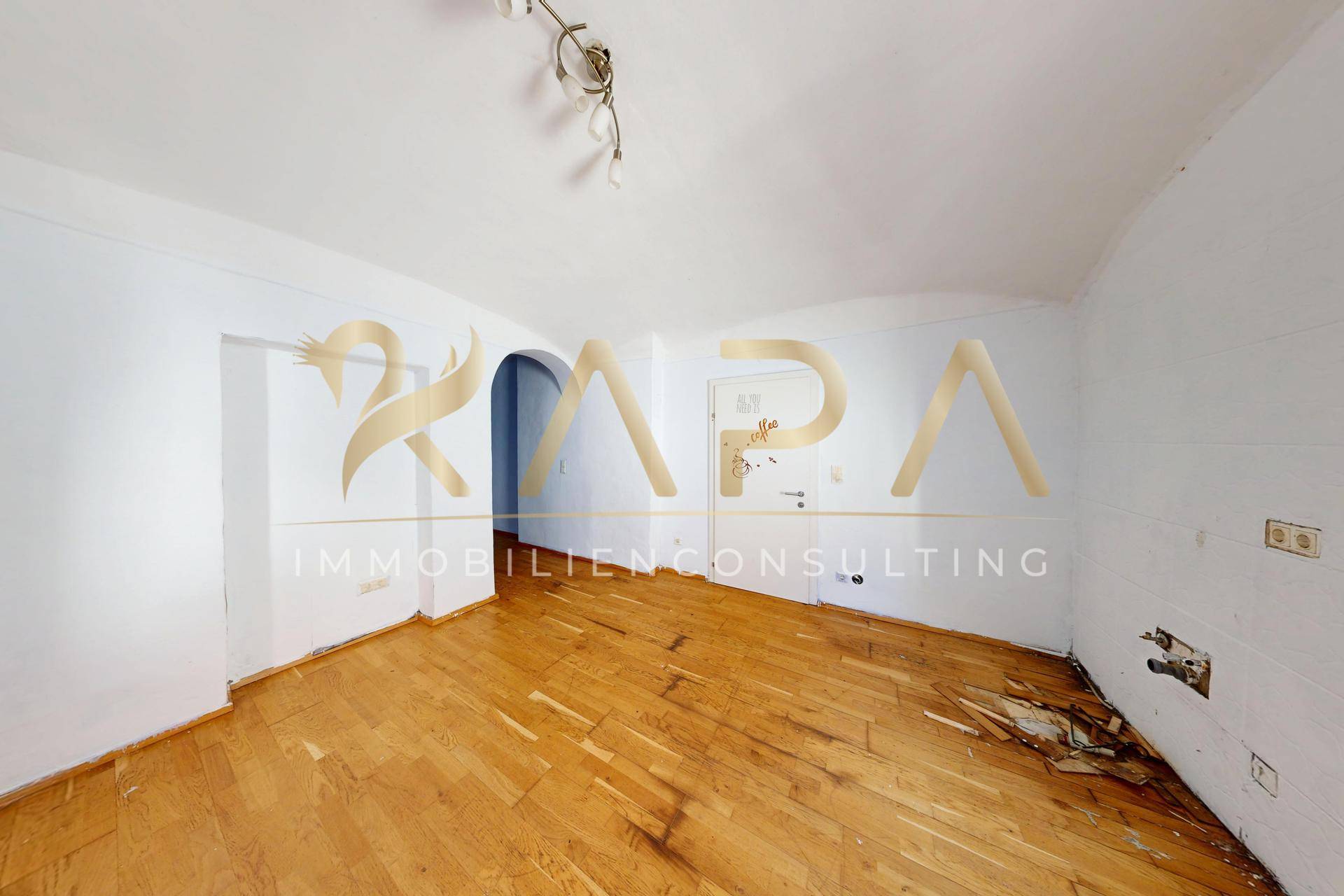 Leerer Raum mit Holzboden und sichtbaren Schäden, benötigt umfassende Renovierung.