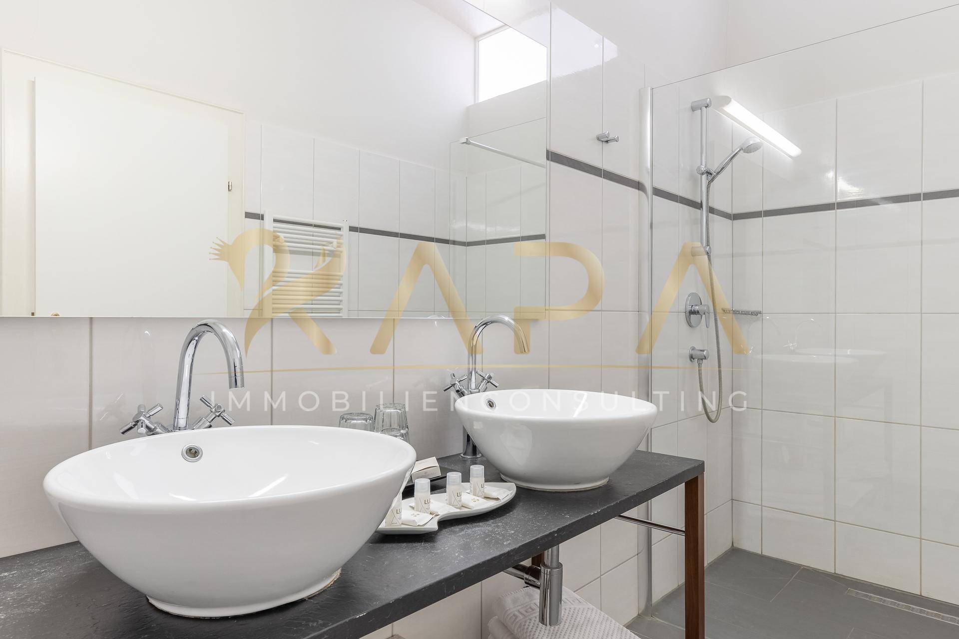 Modernes Badezimmer mit Doppelwaschbecken, großer Dusche und weißen Fliesen.