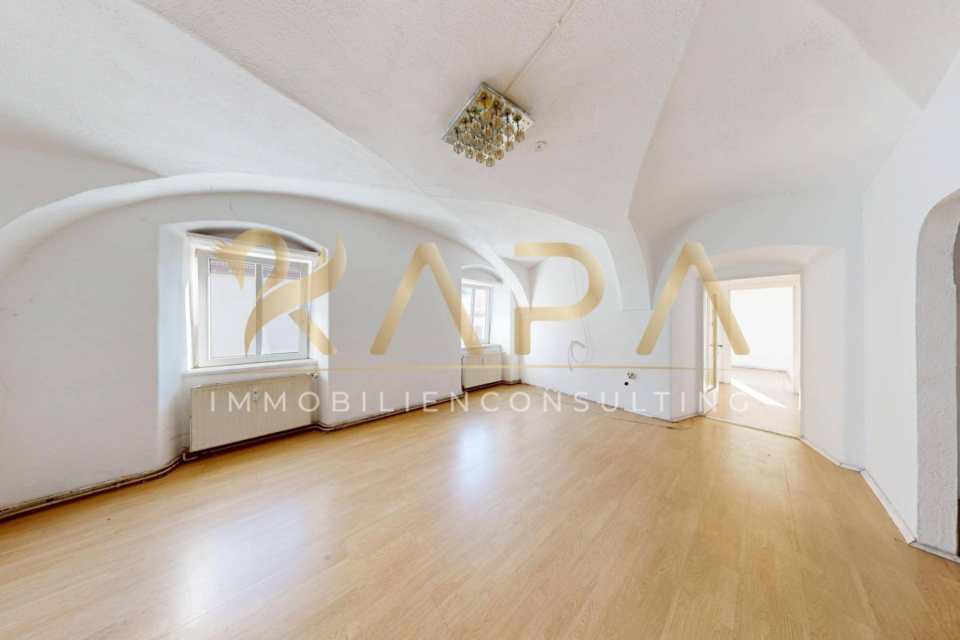 Heller Raum mit beeindruckender Gewölbedecke, Holzparkettboden und großen Fenstern.