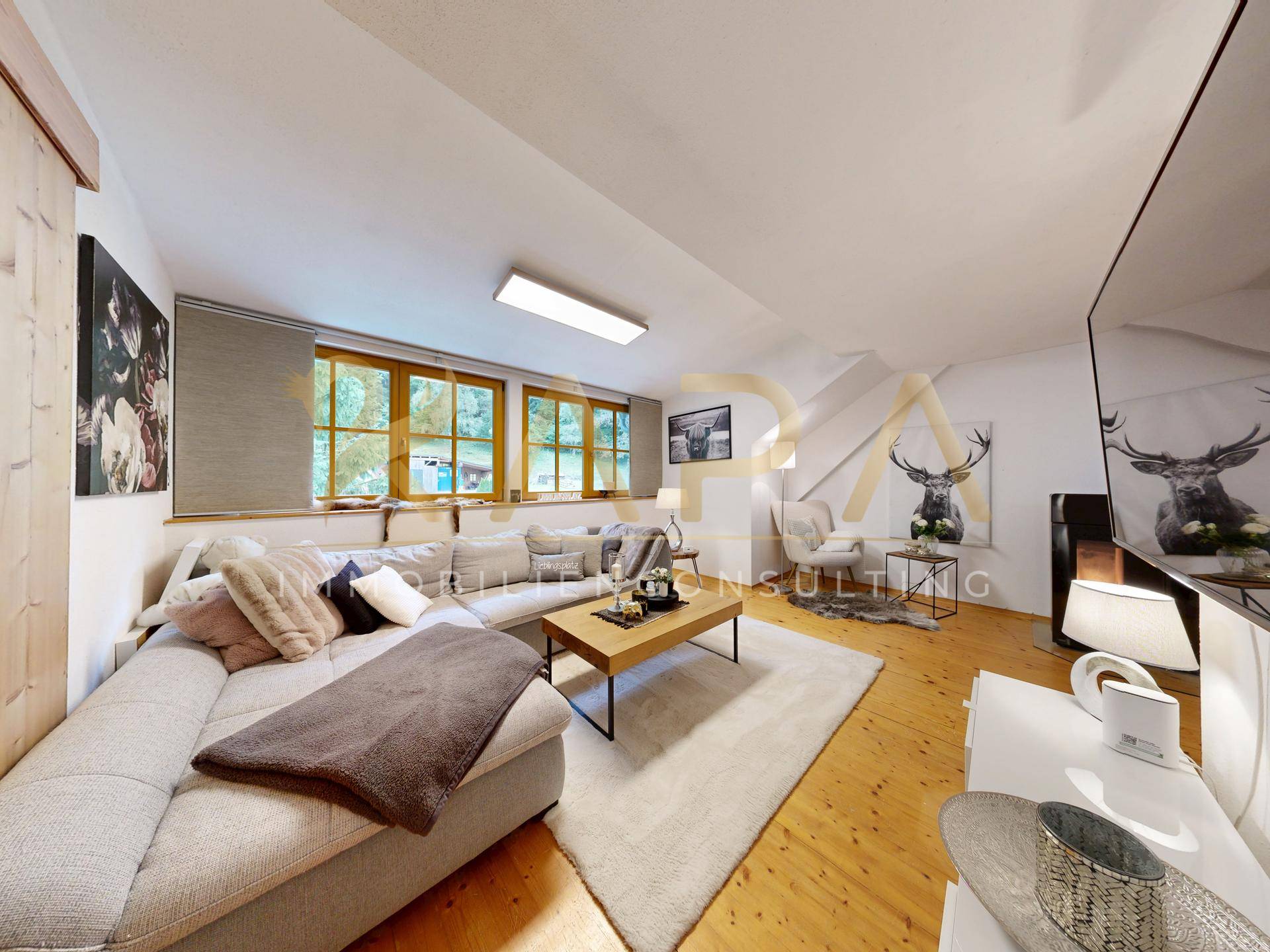 Gemütliches Wohnzimmer im Dachgeschoss mit Holzboden, großem Sofa und schrägen Wänden unter dem Dach.