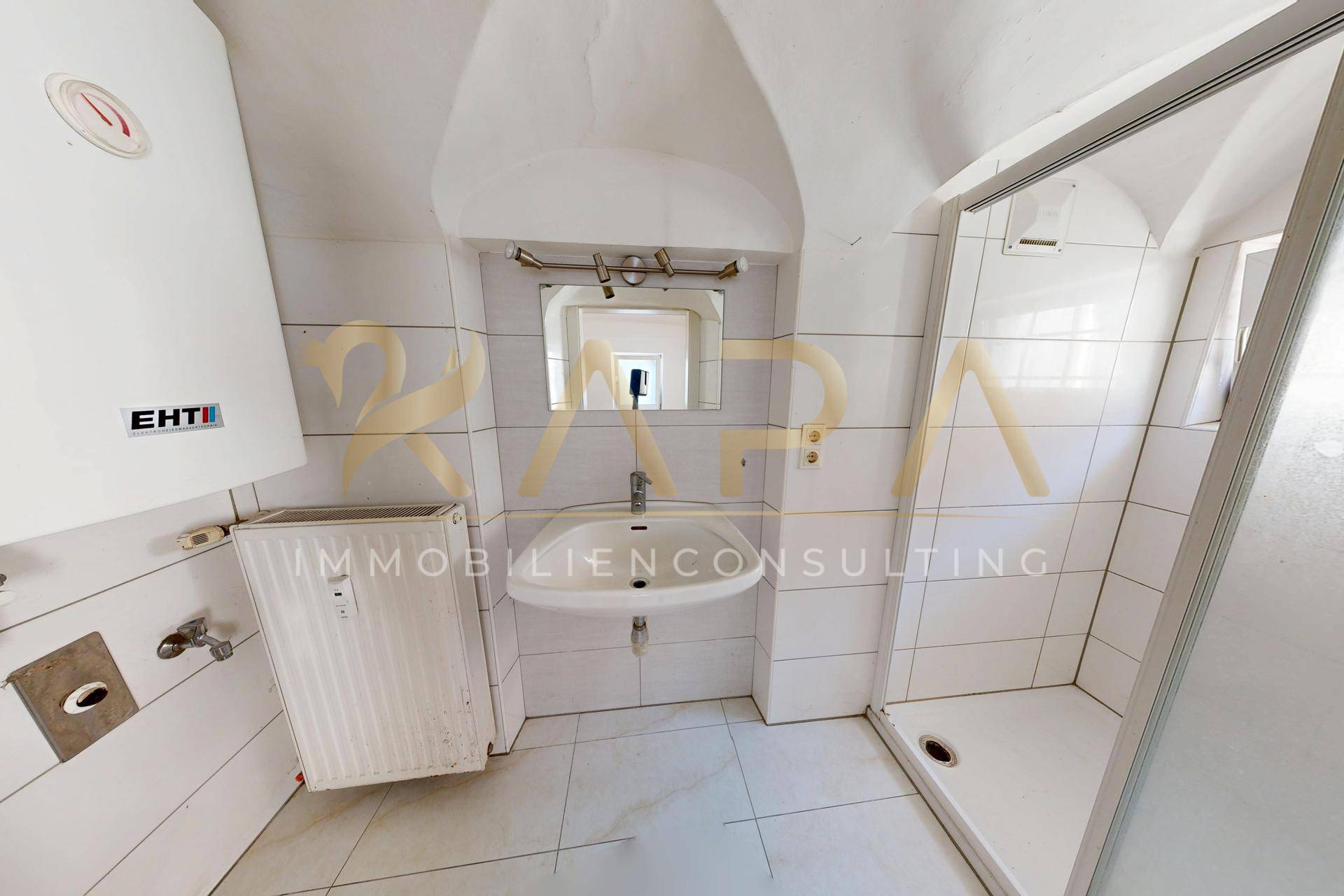 Badezimmer mit Dusche, Waschbecken und Boiler, gefliest und einfach ausgestattet.