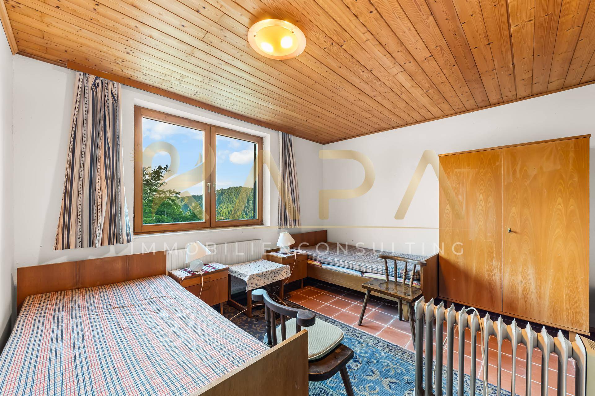 Schlafzimmer mit zwei Einzelbetten, Holzdecke und Blick auf die grüne Landschaft durch das Fenster.