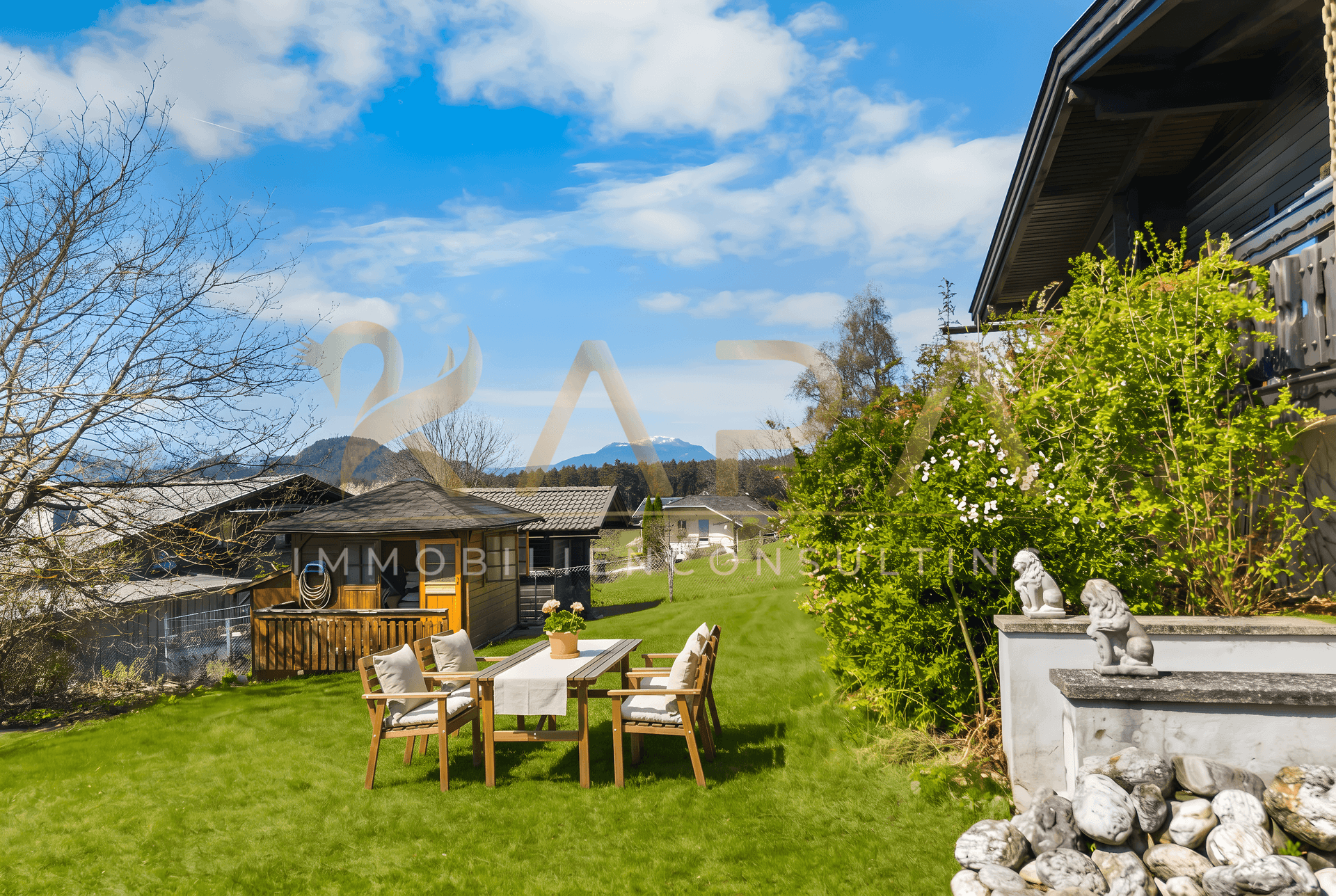 Idyllischer Garten mit Esstisch und Gartenhaus, umgeben von grüner Landschaft und Bergen.