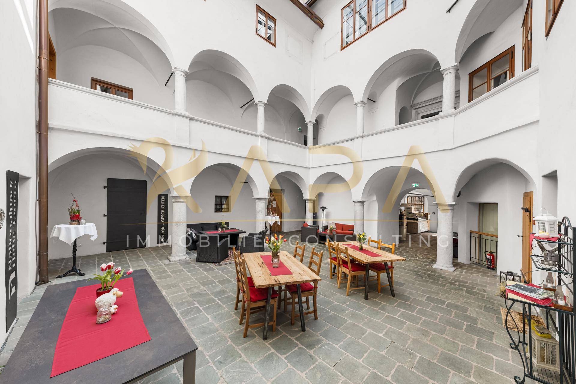 Heller Innenhof mit Arkaden, möbliert mit Tischen und Sitzgelegenheiten für Gäste.