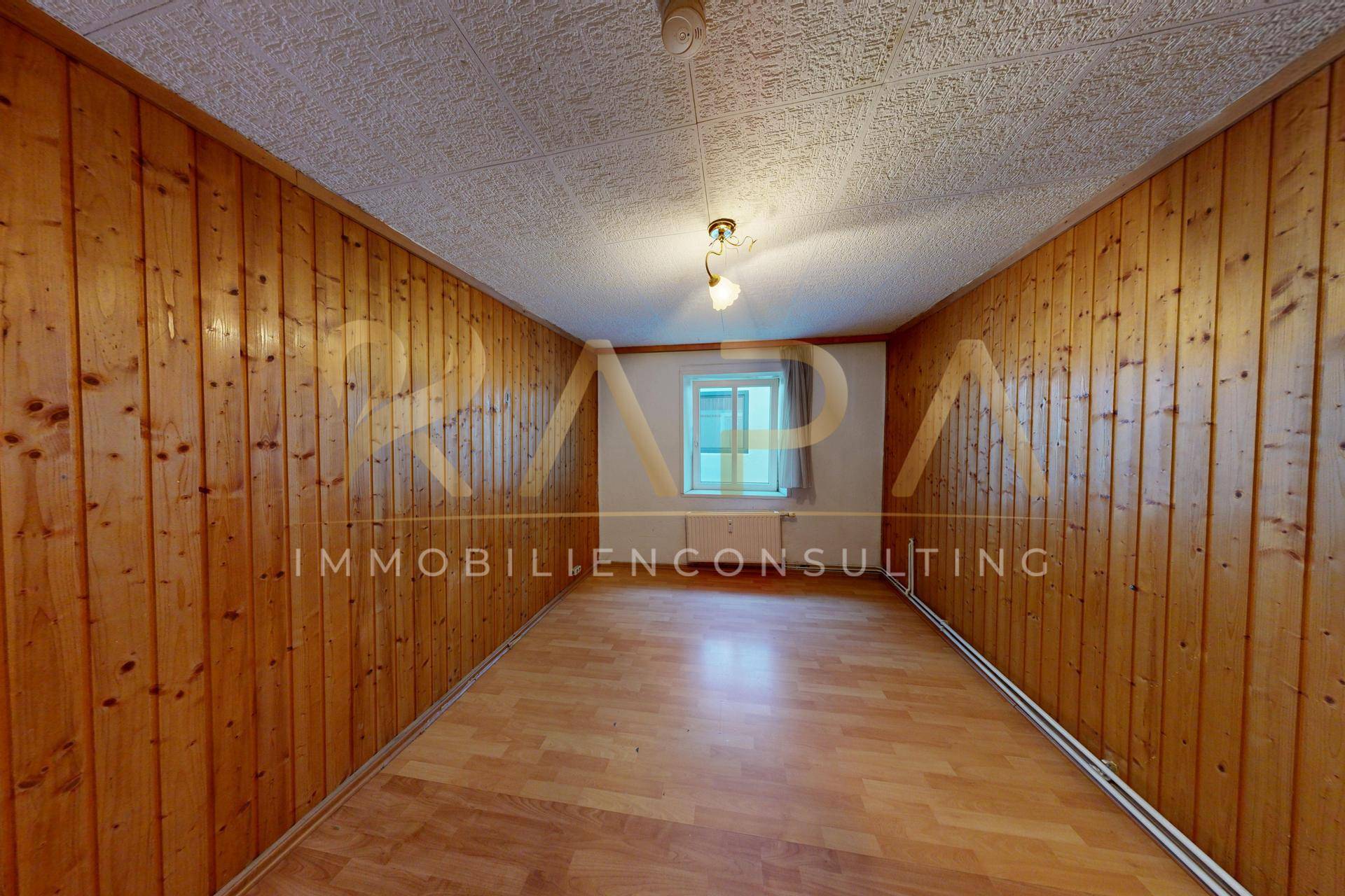 Schlafzimmer mit Holzvertäfelung an den Wänden und Holzboden, einfach eingerichtet.