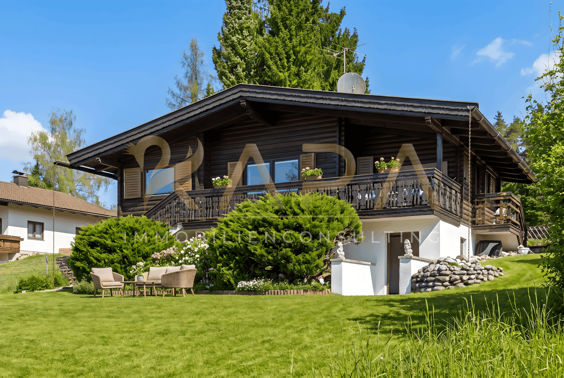 Holzhaus mit kleiner möblierter Sitzecke im Garten und gepflegter Bepflanzung.