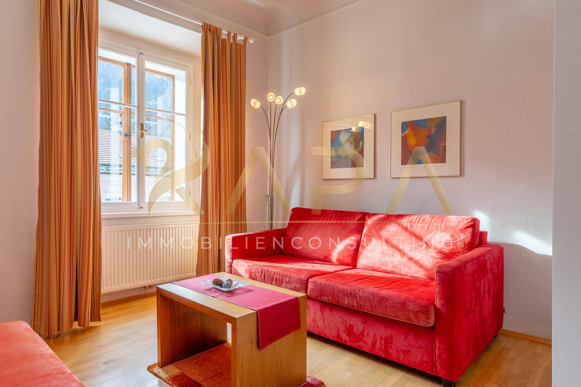 Wohnzimmer mit rotem Sofa, Holzboden und einem Fenster, das viel Tageslicht hereinlässt.