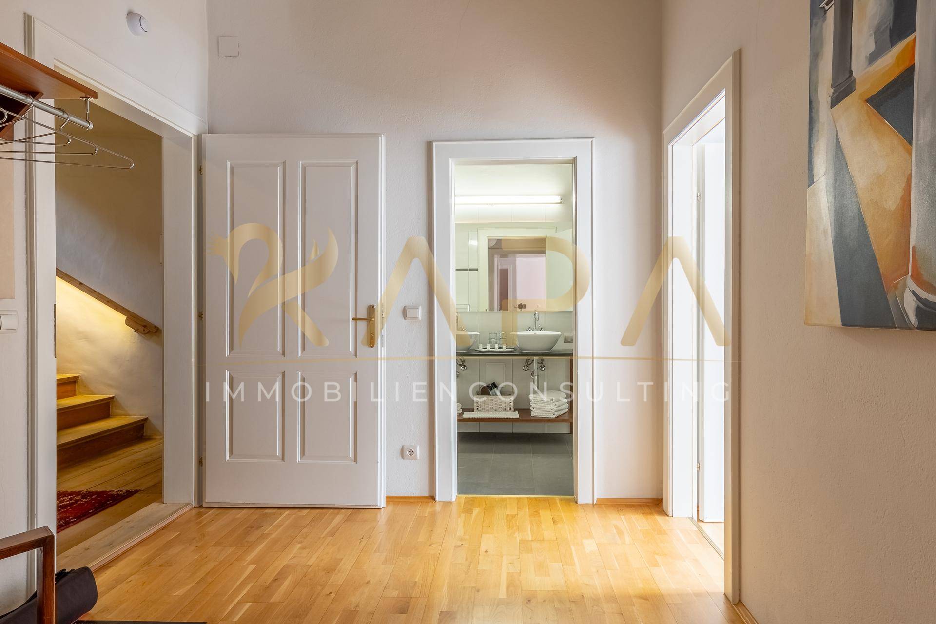 Heller Flur mit Holzboden, der zu einem Badezimmer und einer Treppe führt.