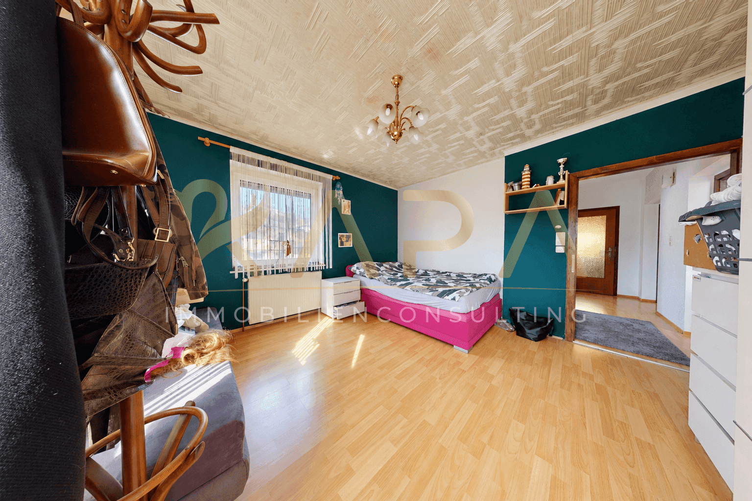 Schlafzimmer mit dunkelgrünen Wänden, Holzboden und einem Bett mit pinker Decke.