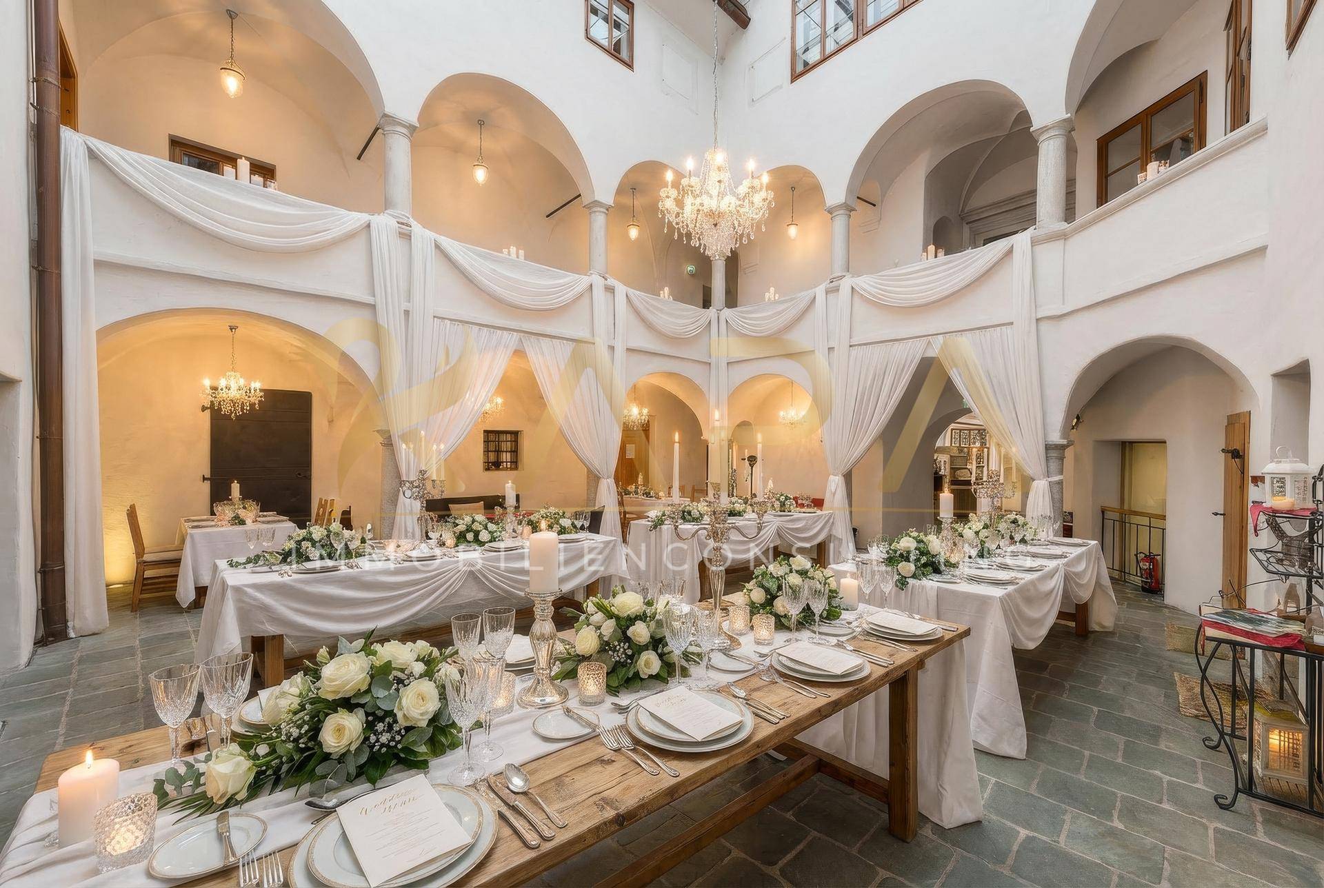 Festlich dekorierter Innenhof mit langen Tischen, Blumenarrangements und Kronleuchter.